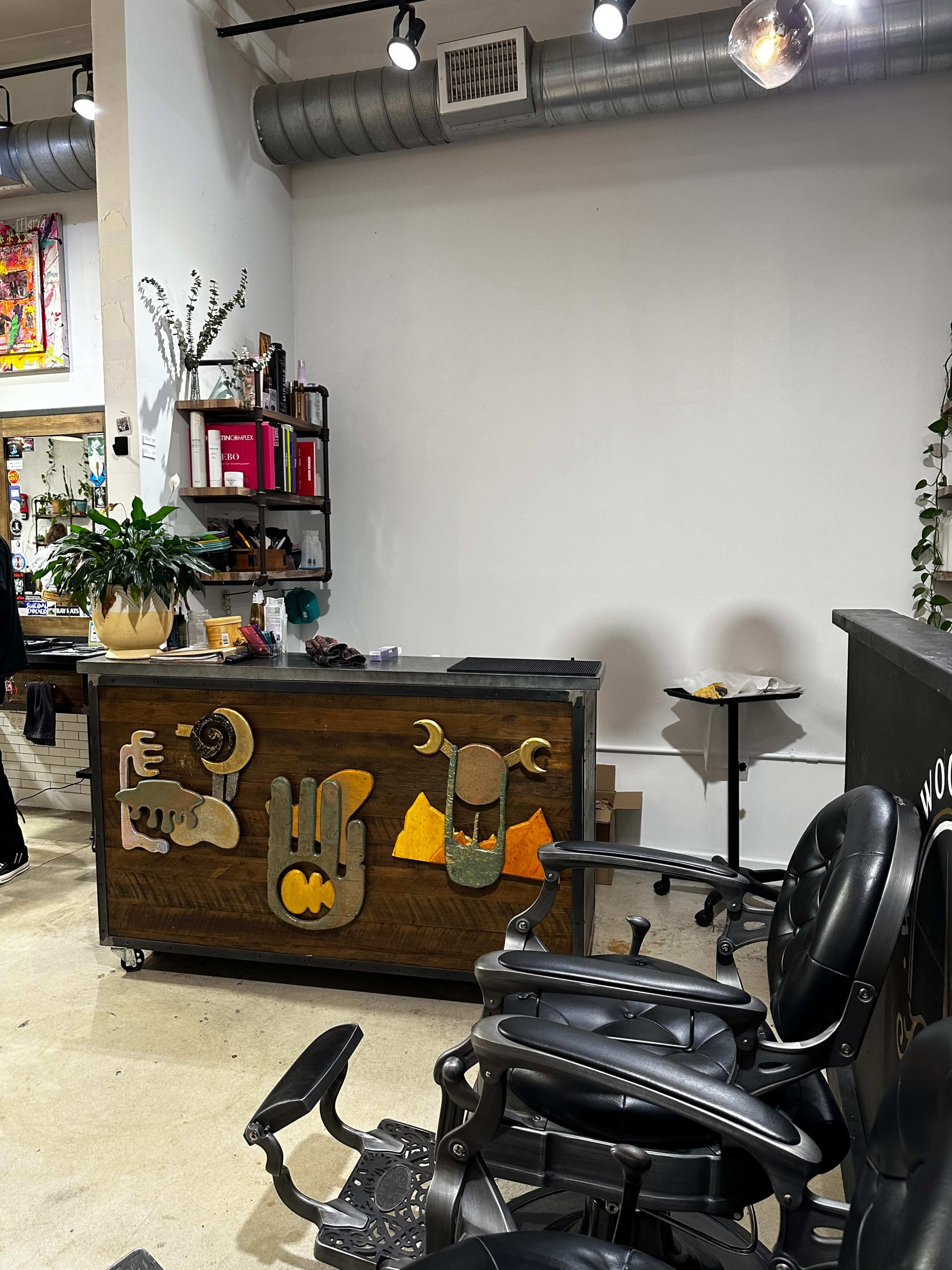 The image shows a beauty salon interior featuring a reception desk with decorative elements and stylized hands, along with black salon chairs in the foreground.