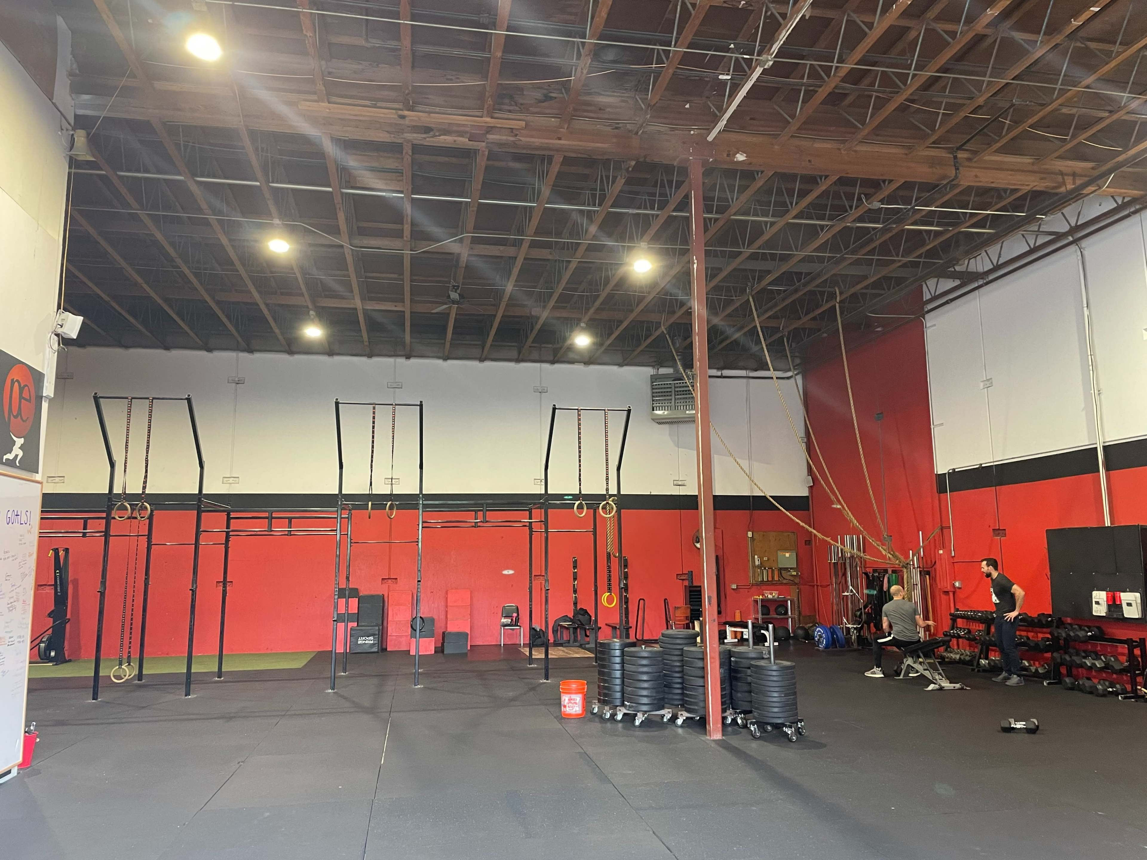 An indoor gym with various workout equipment, including weights and exercise bars, set against red and black walls.