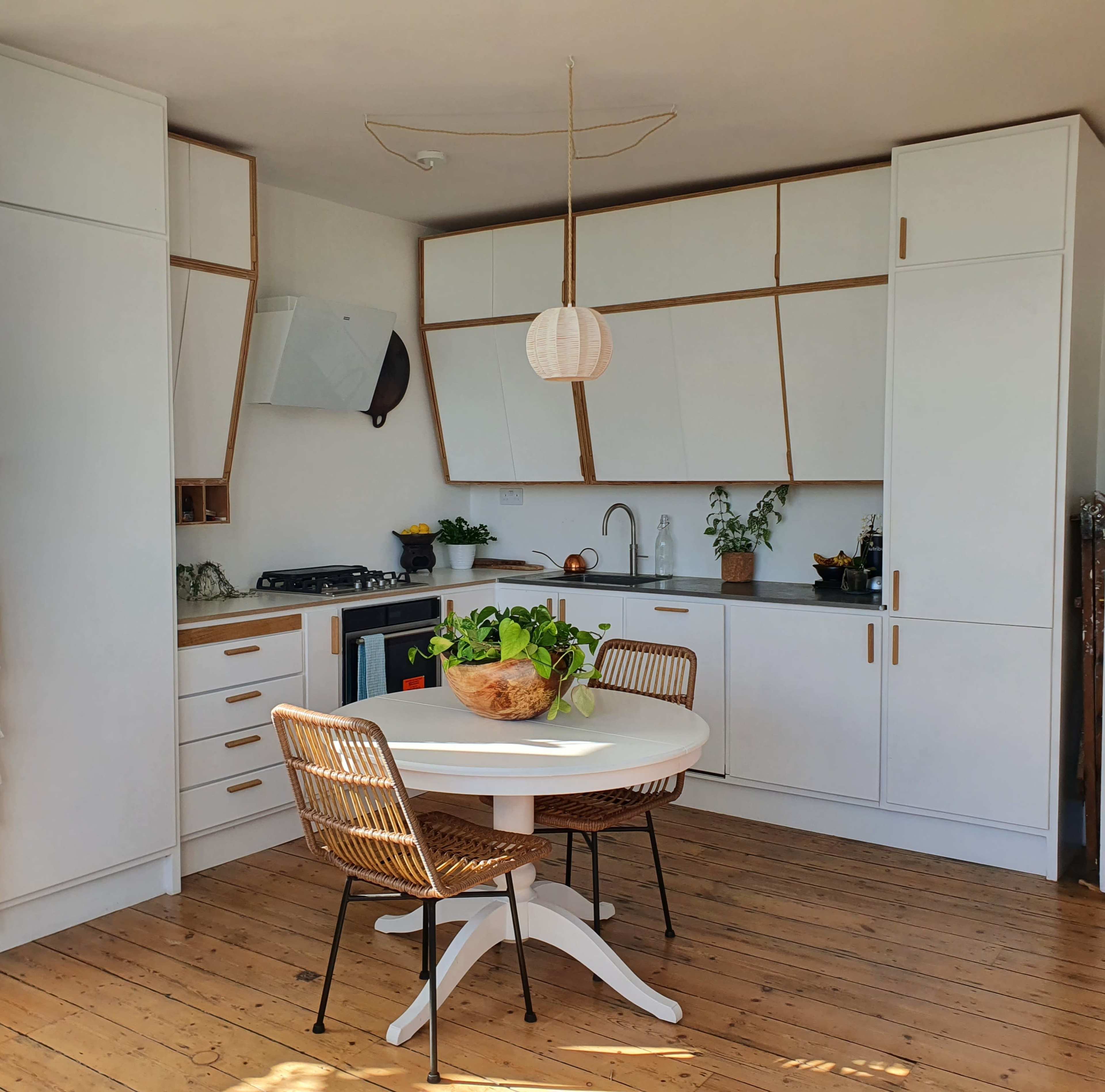 A modern kitchen with white cabinets, wooden accents, a round dining table, and two woven chairs.