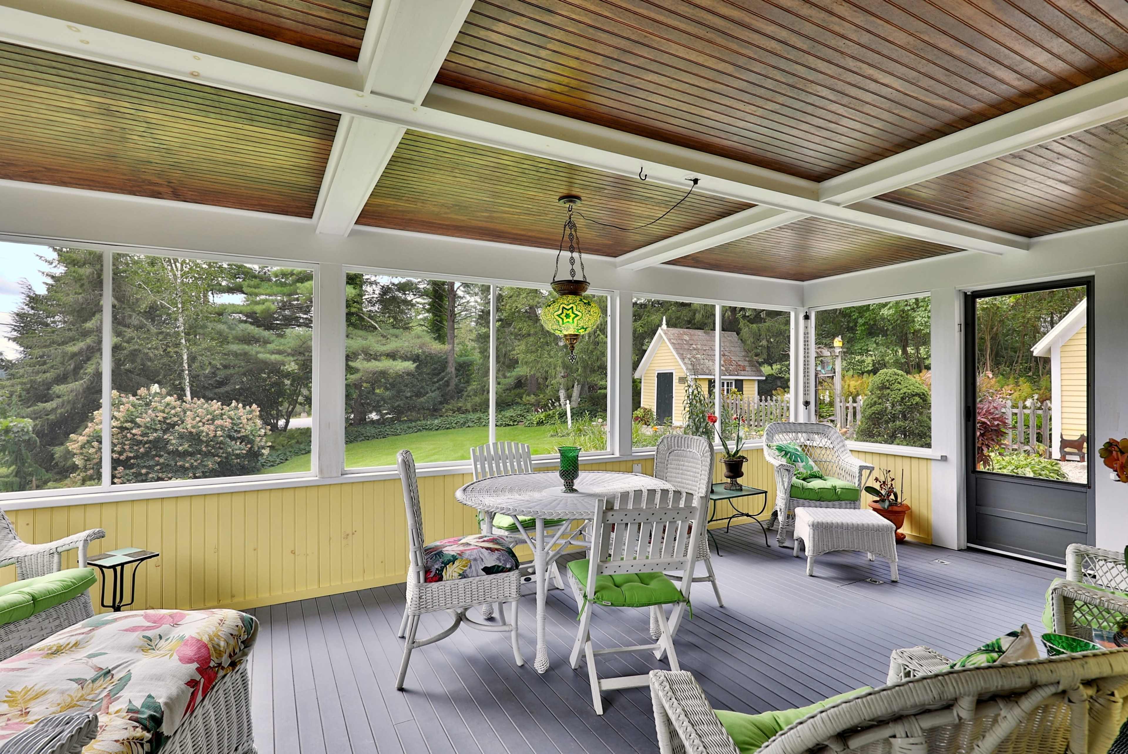 A screened-in porch with wicker furniture, a round table, and a green lawn visible through the open screens.