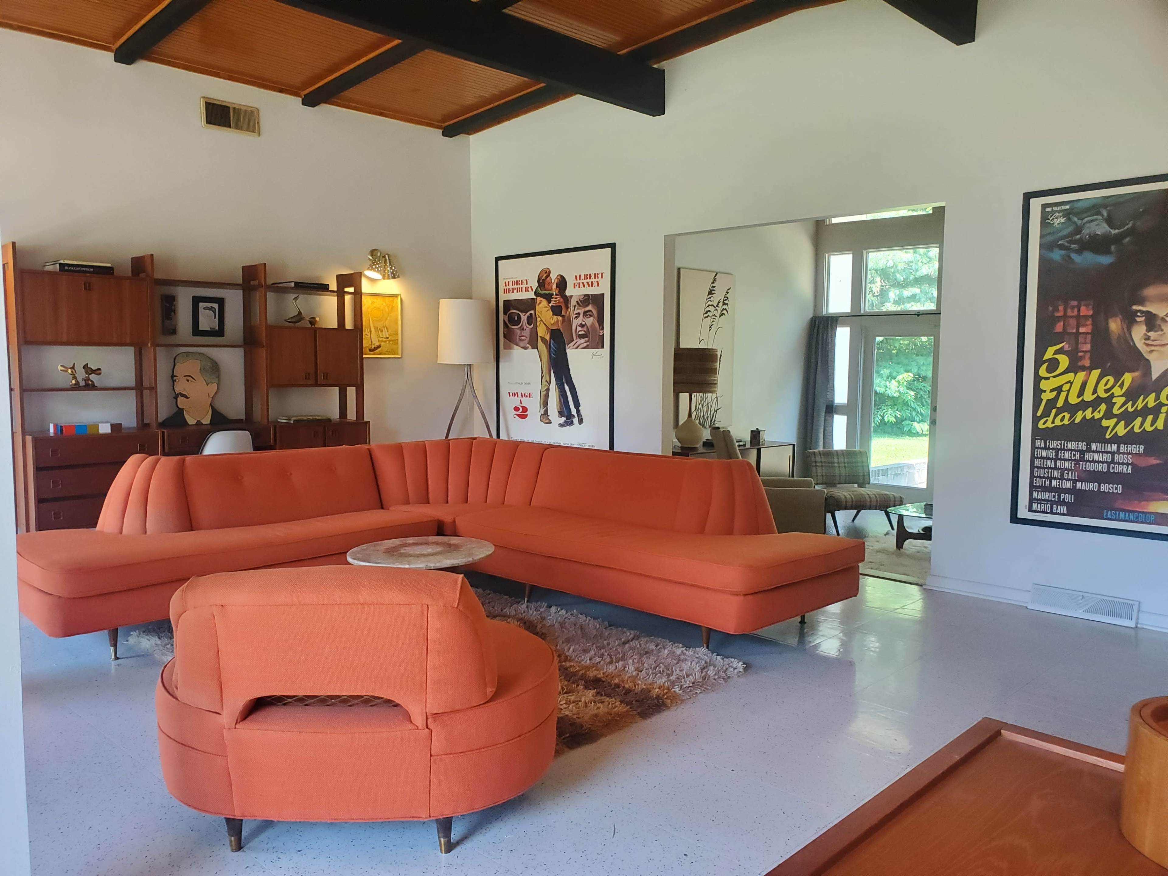 A modern living room with an orange sectional sofa, a round coffee table, artwork on the walls, and large windows providing natural light.