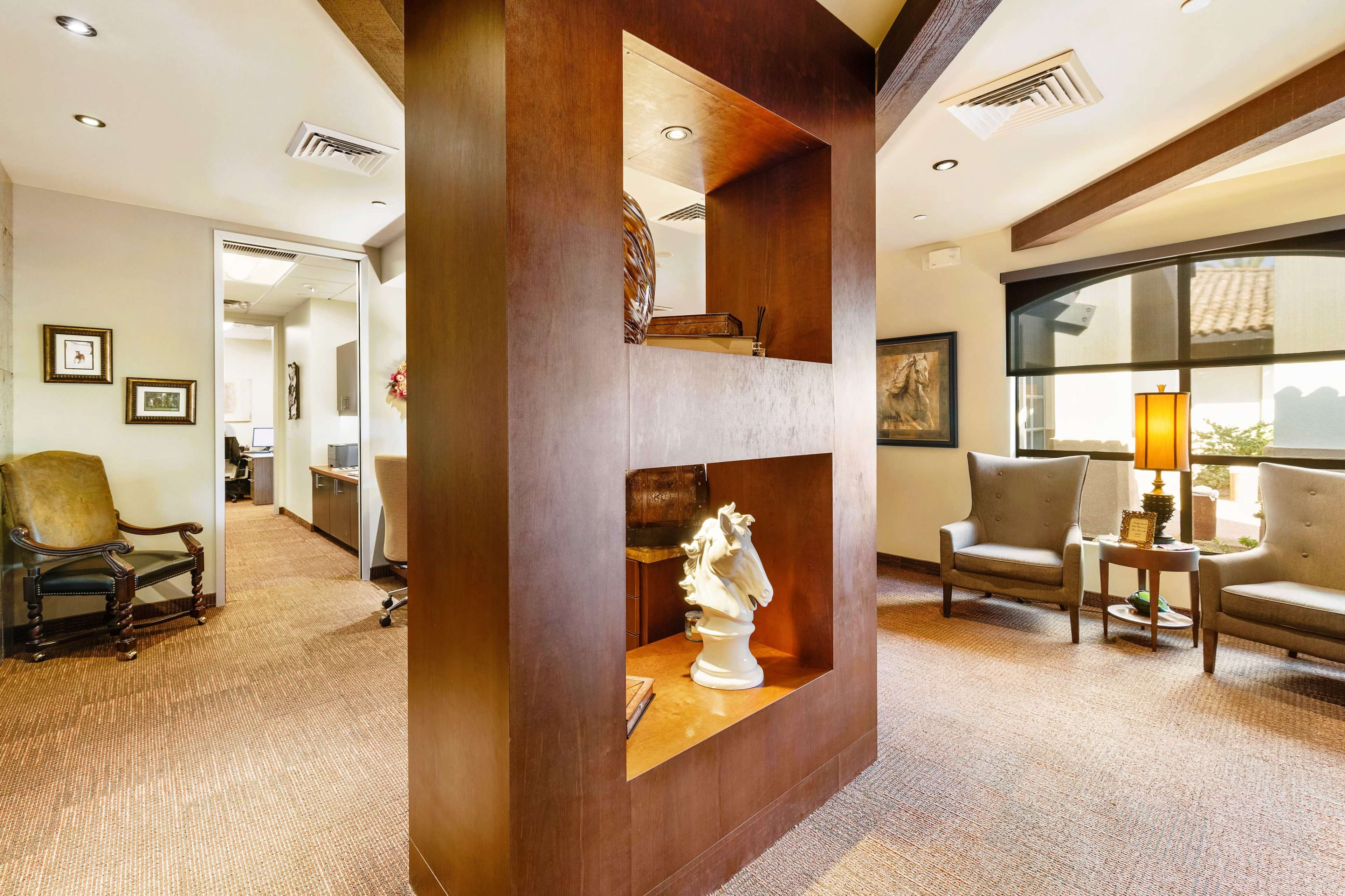 The image shows a modern office reception area with a wooden display unit, plush seating, and framed artwork.