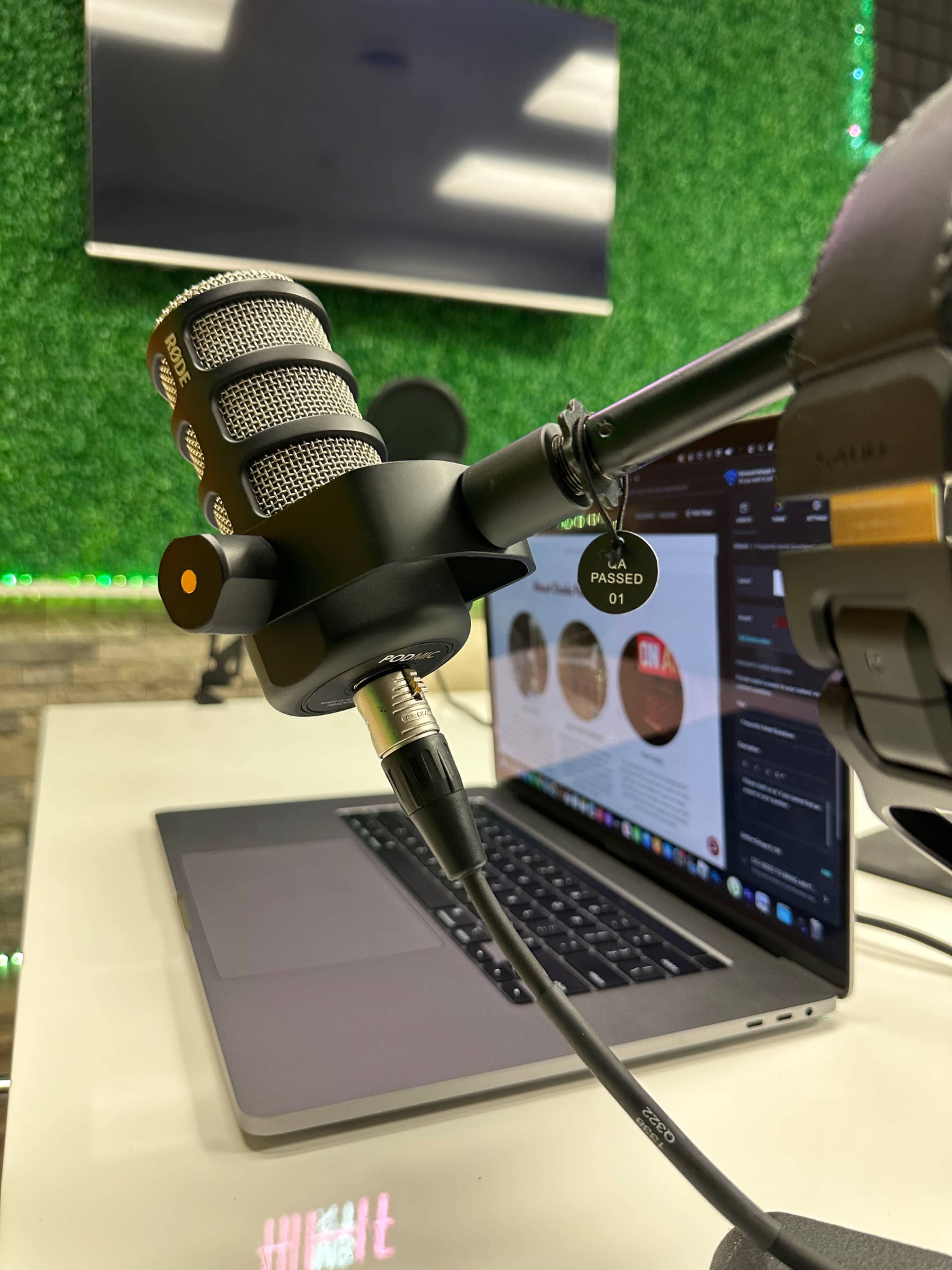 A microphone is mounted on an arm next to a laptop displaying various screens in a studio setting with green walls.