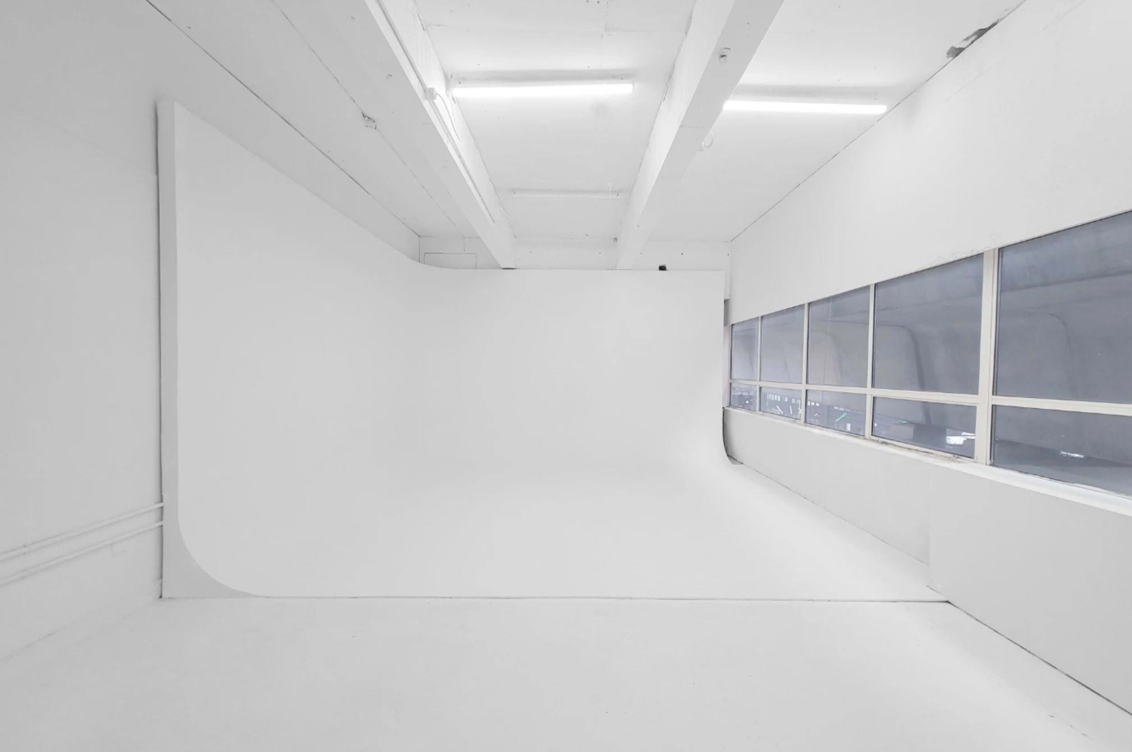 The image shows a spacious photography studio with a seamless white backdrop and a large window.