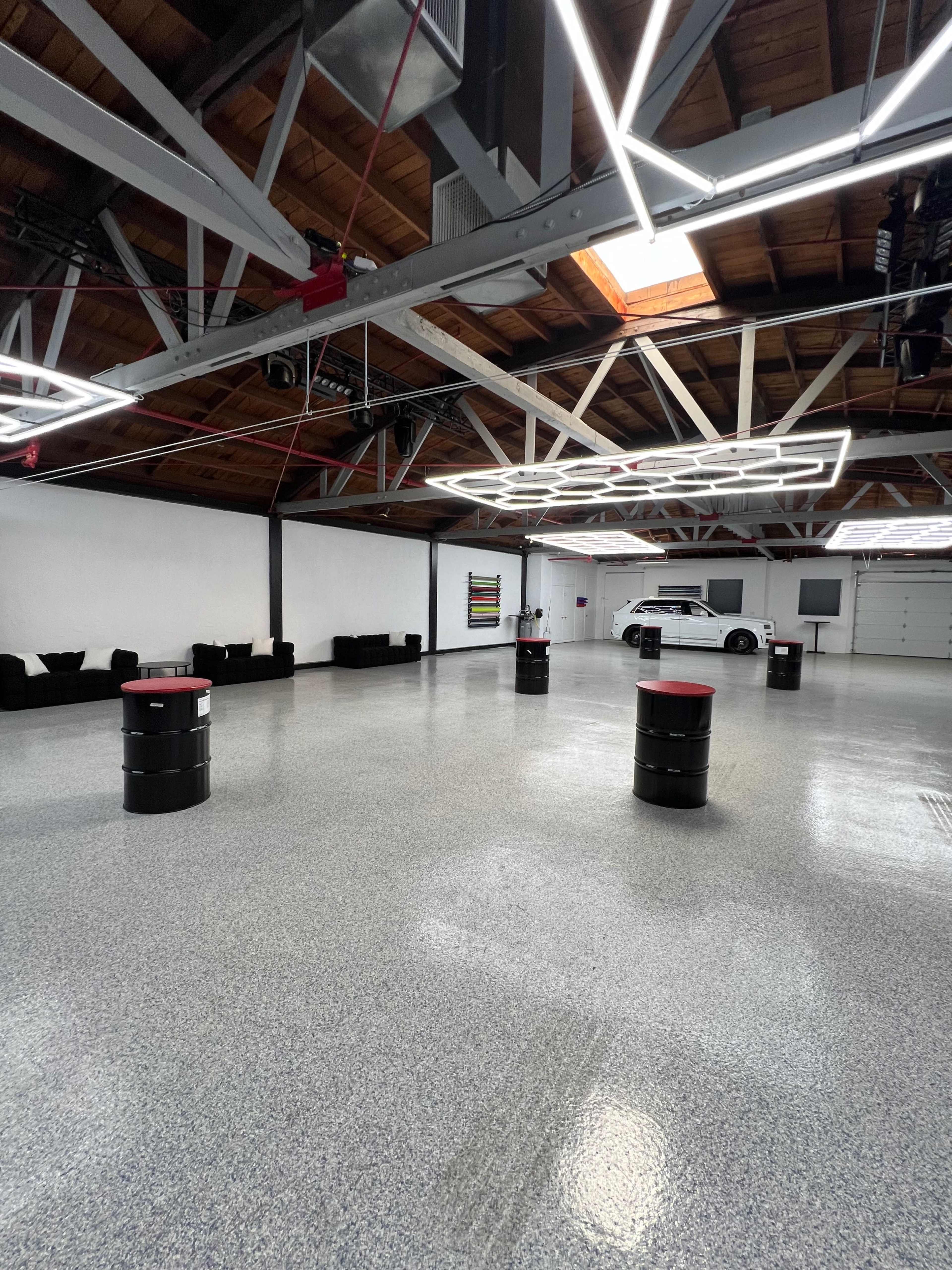 A spacious garage with a polished floor, black barrels with red tops, and modern lighting fixtures.