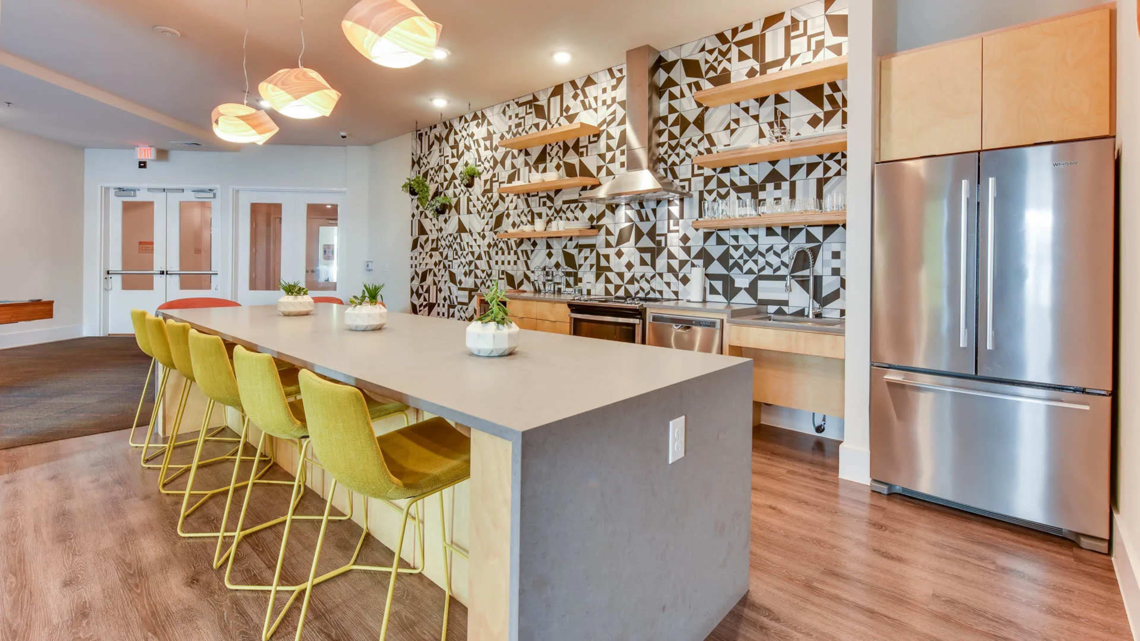 The image shows a modern kitchen with a geometric-patterned backsplash, a central island with yellow bar stools, and stainless steel appliances.