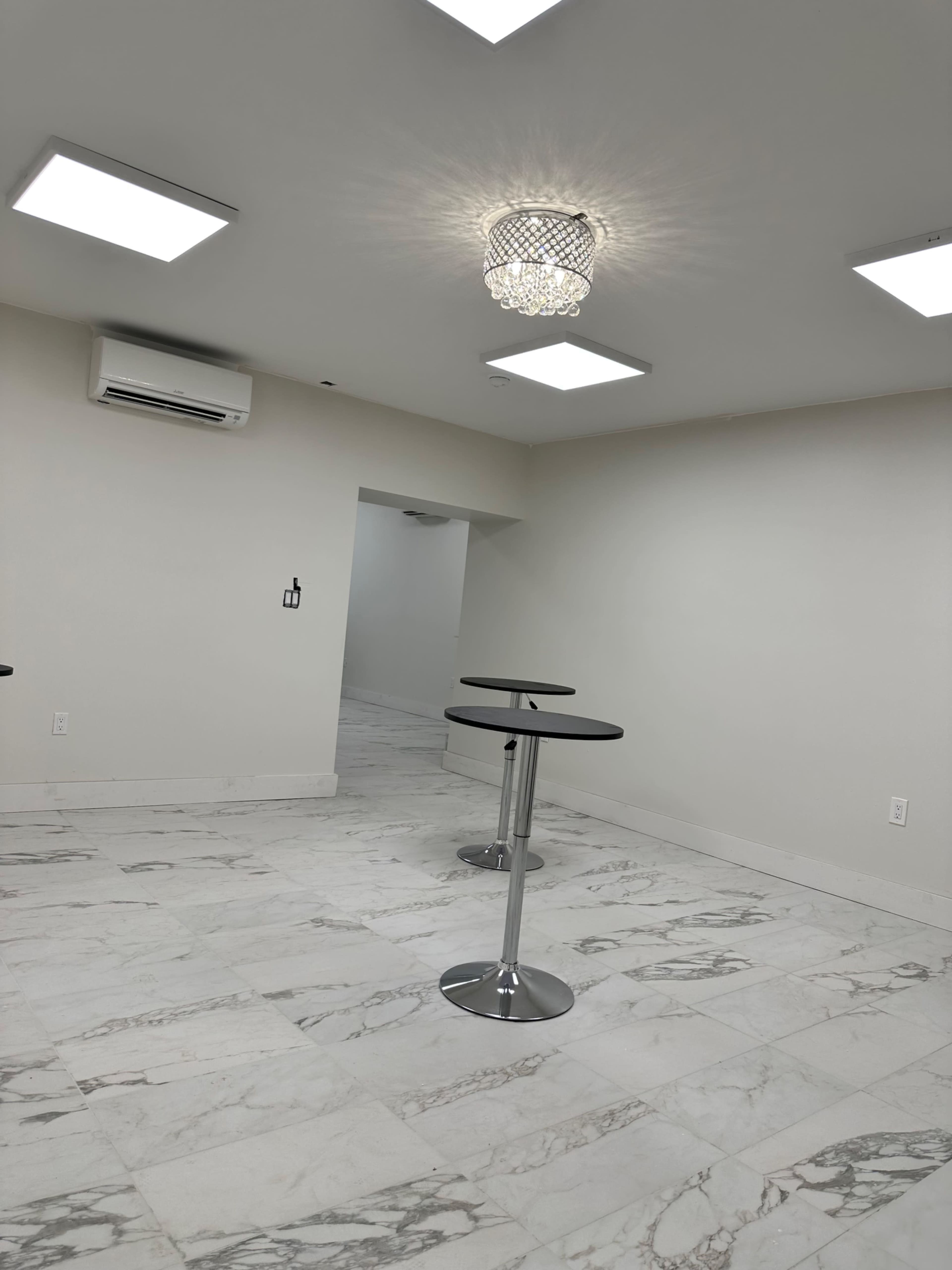 A minimalist room with marble flooring, featuring two high-top tables and modern ceiling lights.