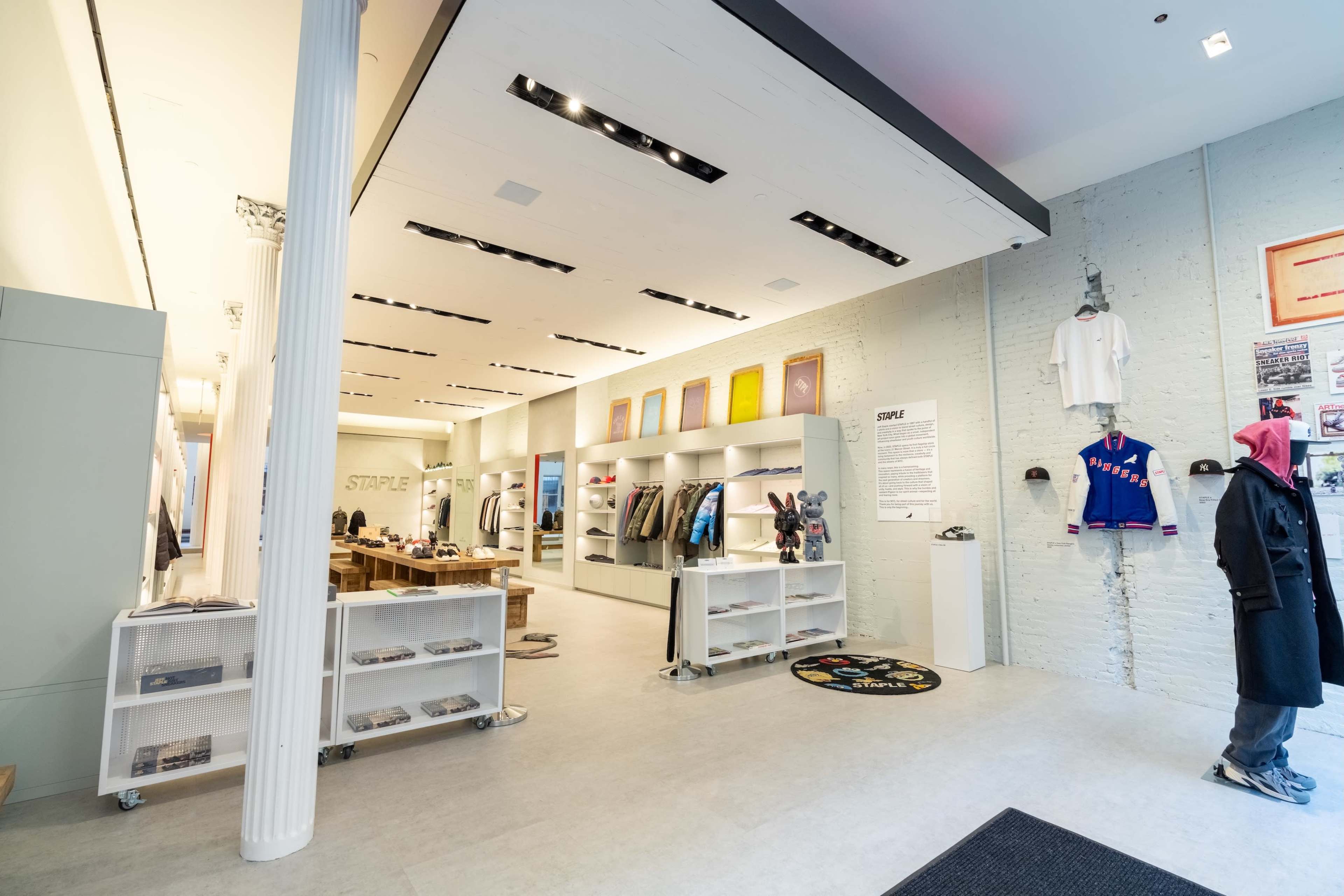 The image shows a modern retail store interior featuring clothing displays, a checkout counter, and wall-mounted garments in a bright, spacious setting.