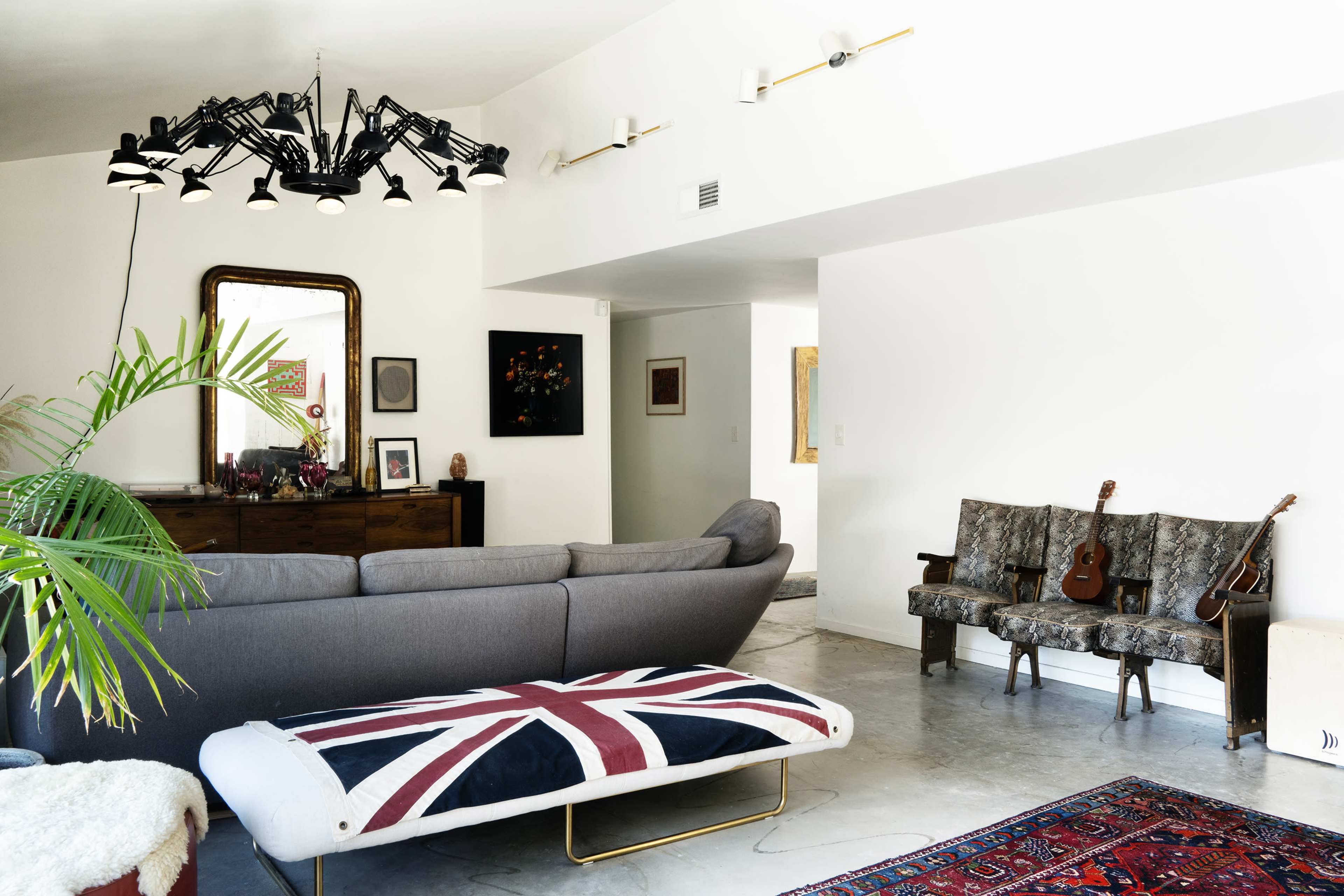 The living room features a gray sectional sofa, a Union Jack-patterned ottoman, and vintage seating with two guitars displayed beside them.