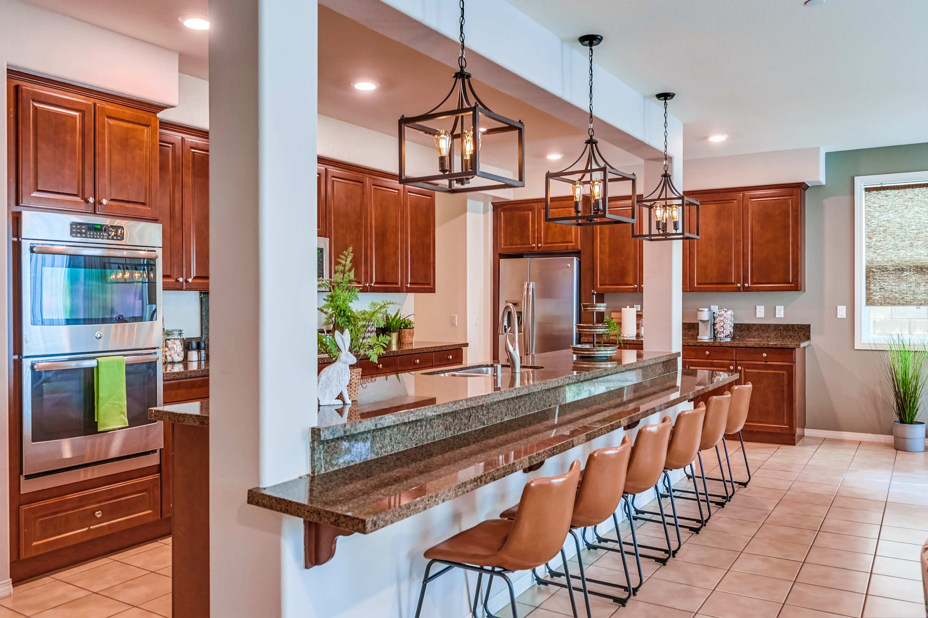 A modern kitchen with wooden cabinets, a central island featuring bar seating, and pendant lights above.