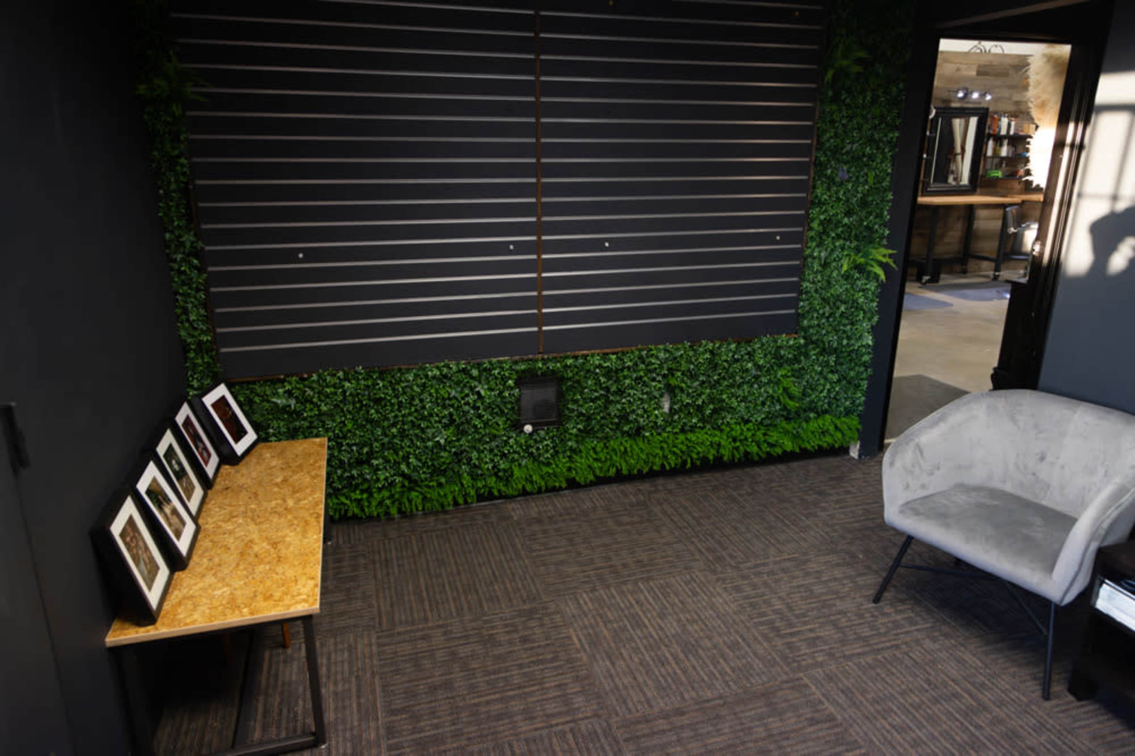 The scene features a small interior space with a wooden bench displaying several framed pictures against a backdrop of artificial greenery and a dark wall.