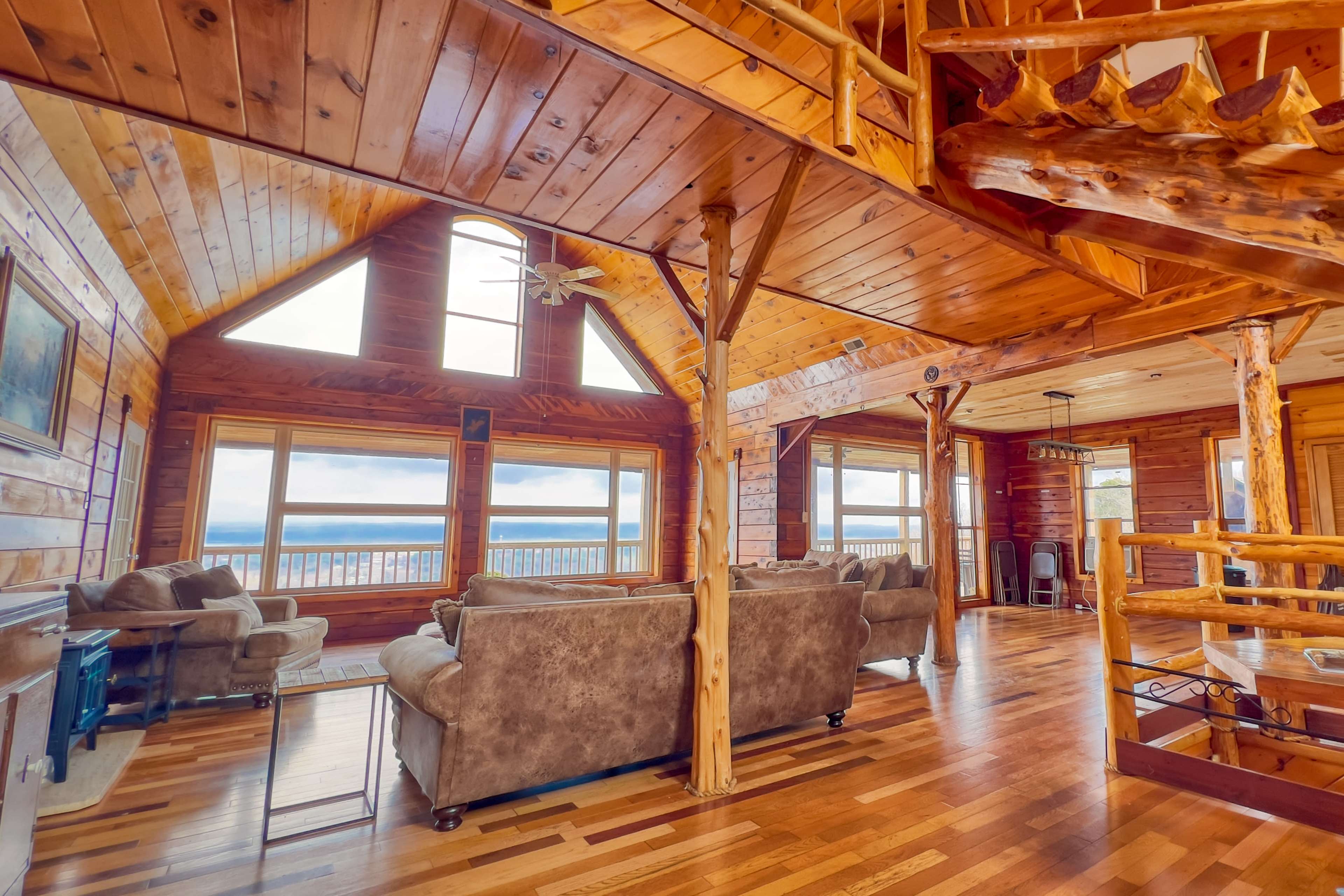 The interior of a spacious wooden cabin features large windows that provide a view of the landscape, with a seating area and wooden beams overhead.