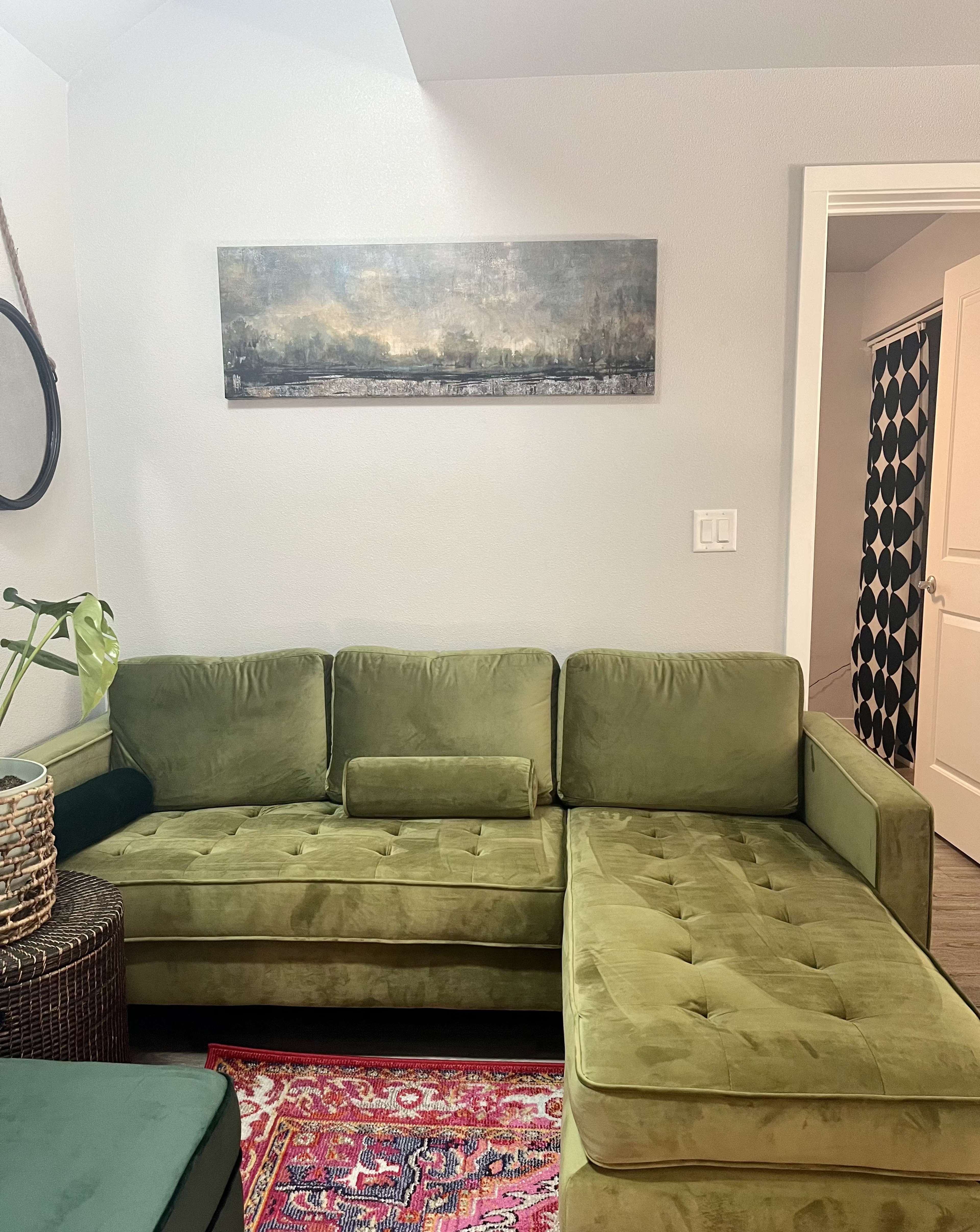 A green sectional sofa in a room with a wall-mounted painting and a patterned door in the background.