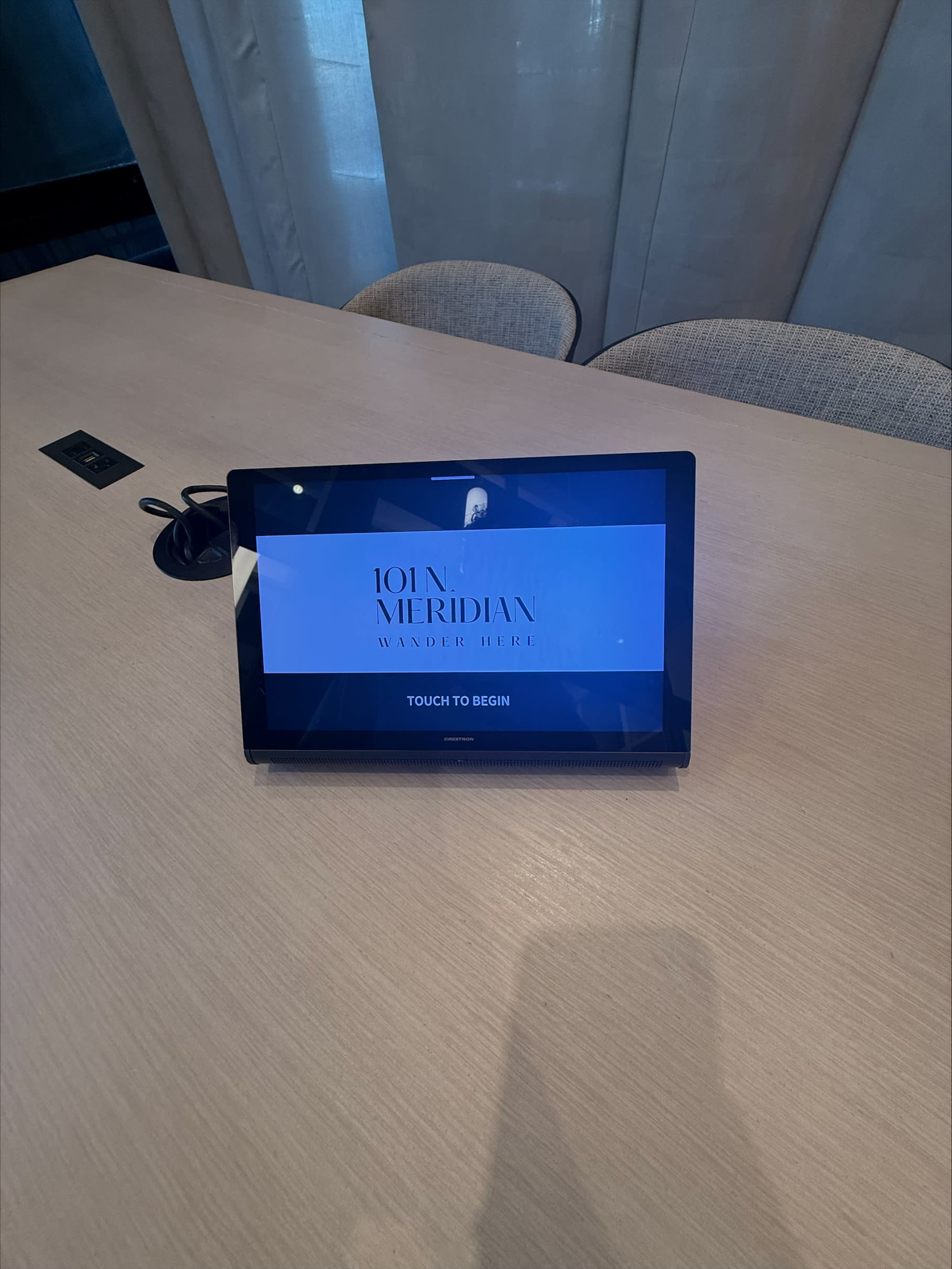 The image shows a touchscreen display with the text "JOHN MERIDIAN WANDER HERE" on a table in a well-lit room.