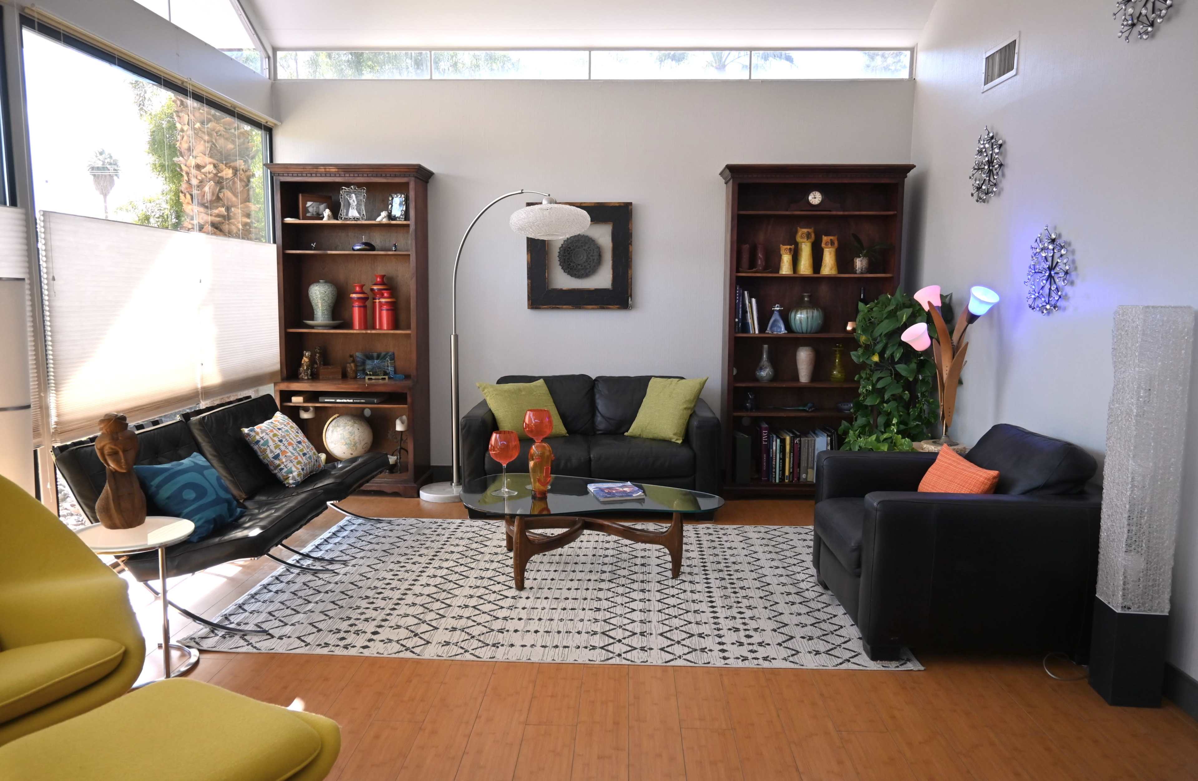 The image shows a modern living room with two seating areas, a coffee table, and shelves displaying decorative items.