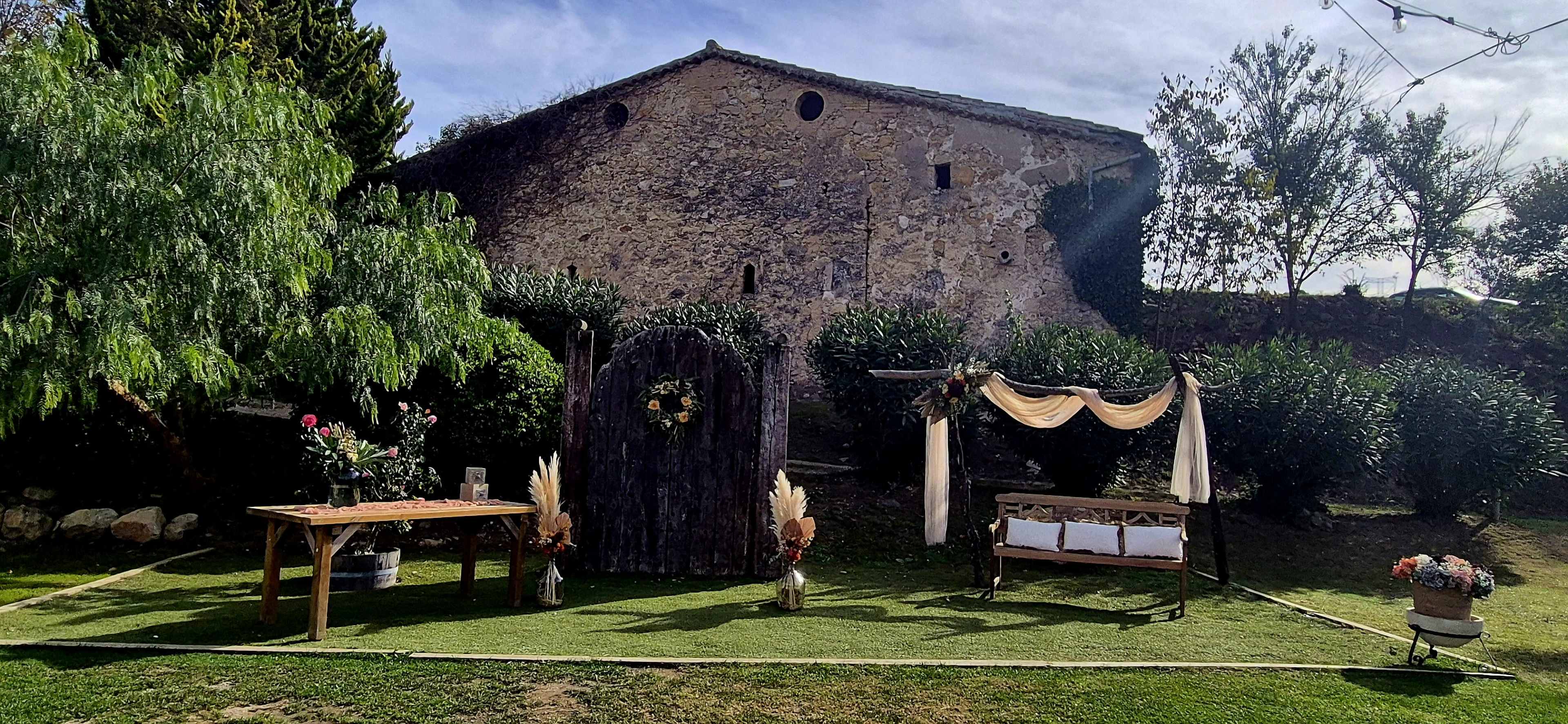 The scene features a decorative outdoor setting with a wooden arch, a table with floral arrangements, and a rustic building in the background.