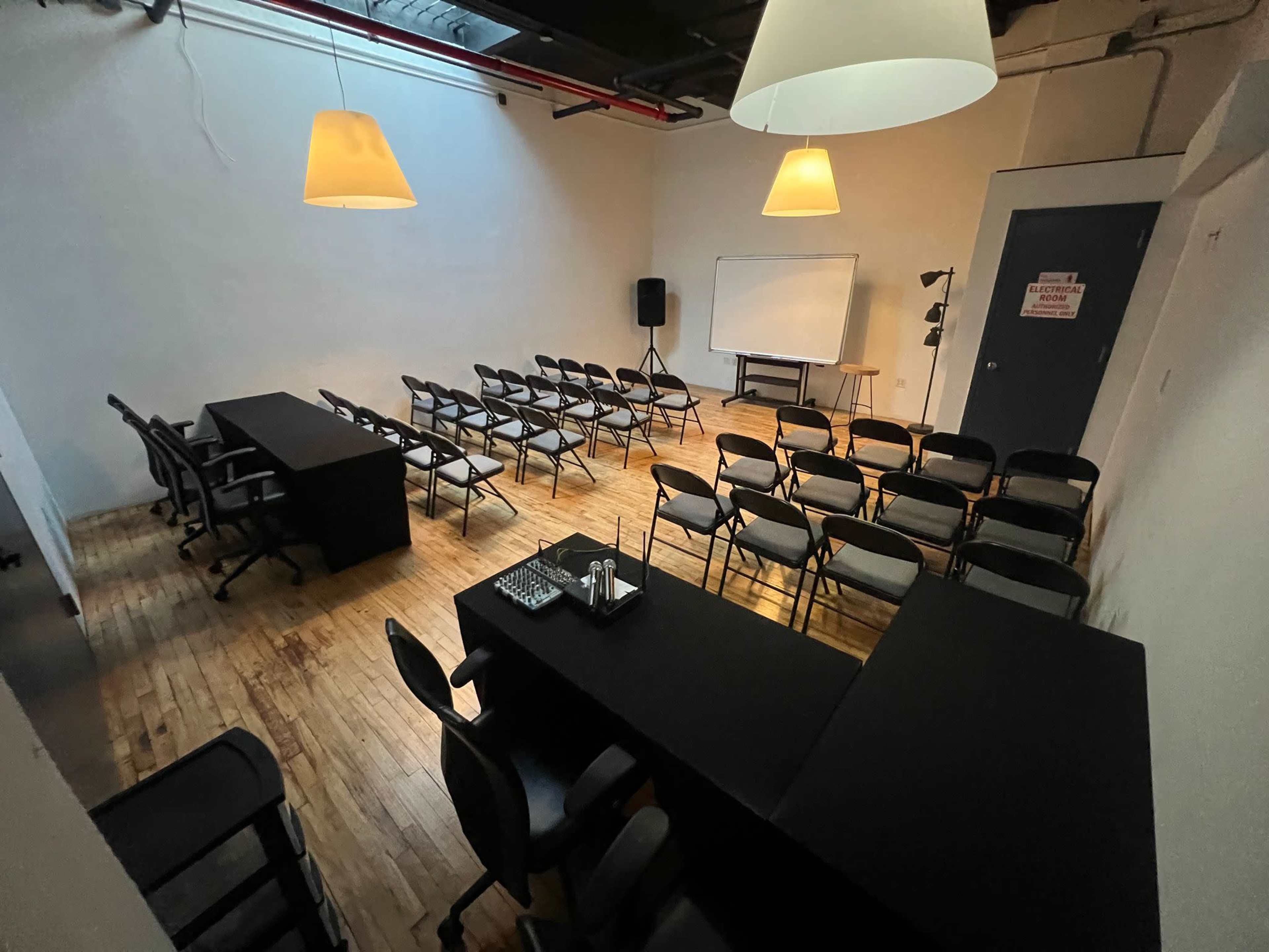 The image shows a spacious, empty room set up for a meeting, featuring a long table at the front, several rows of chairs, and a whiteboard on one side.