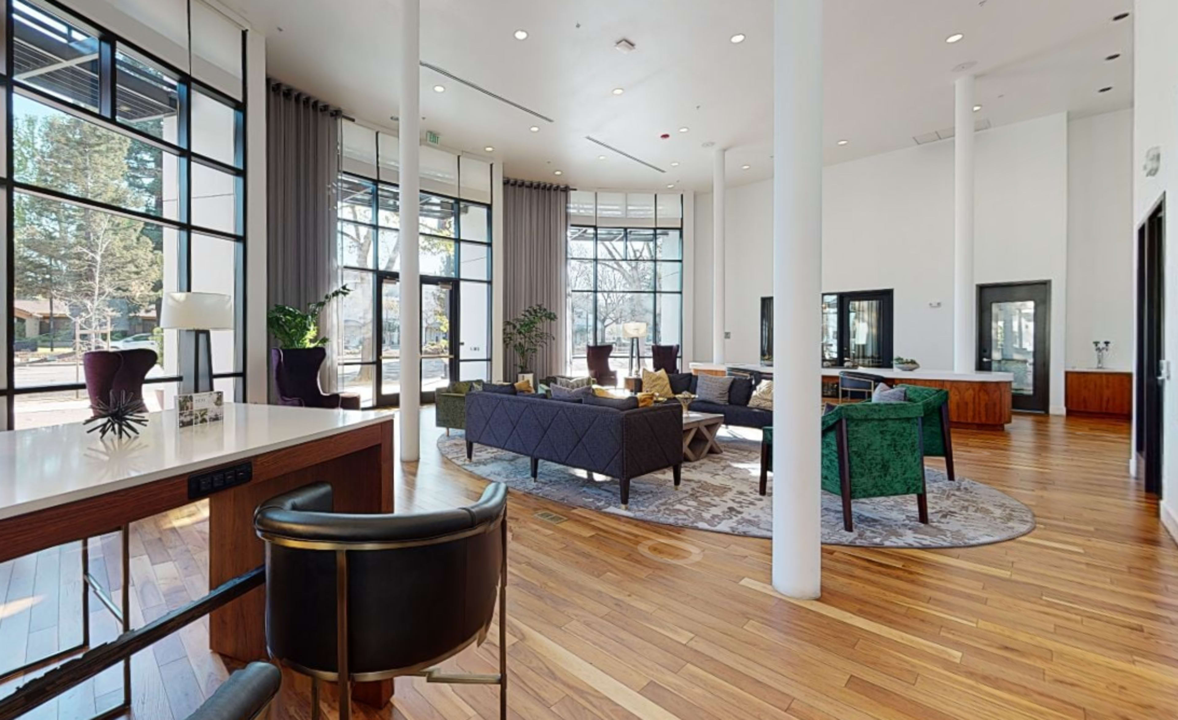 A spacious, well-lit living area with large windows, modern furniture, and wooden flooring.