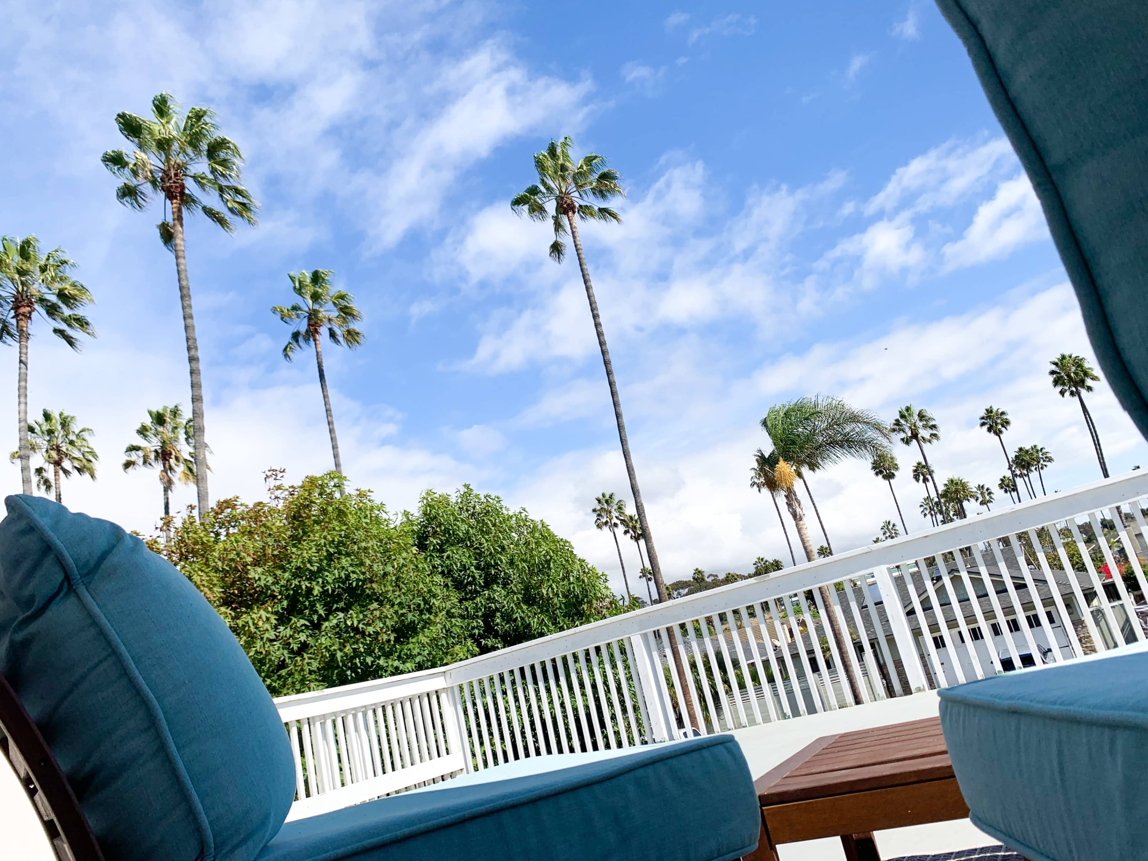 A view from a balcony featuring tall palm trees and a partly cloudy blue sky.