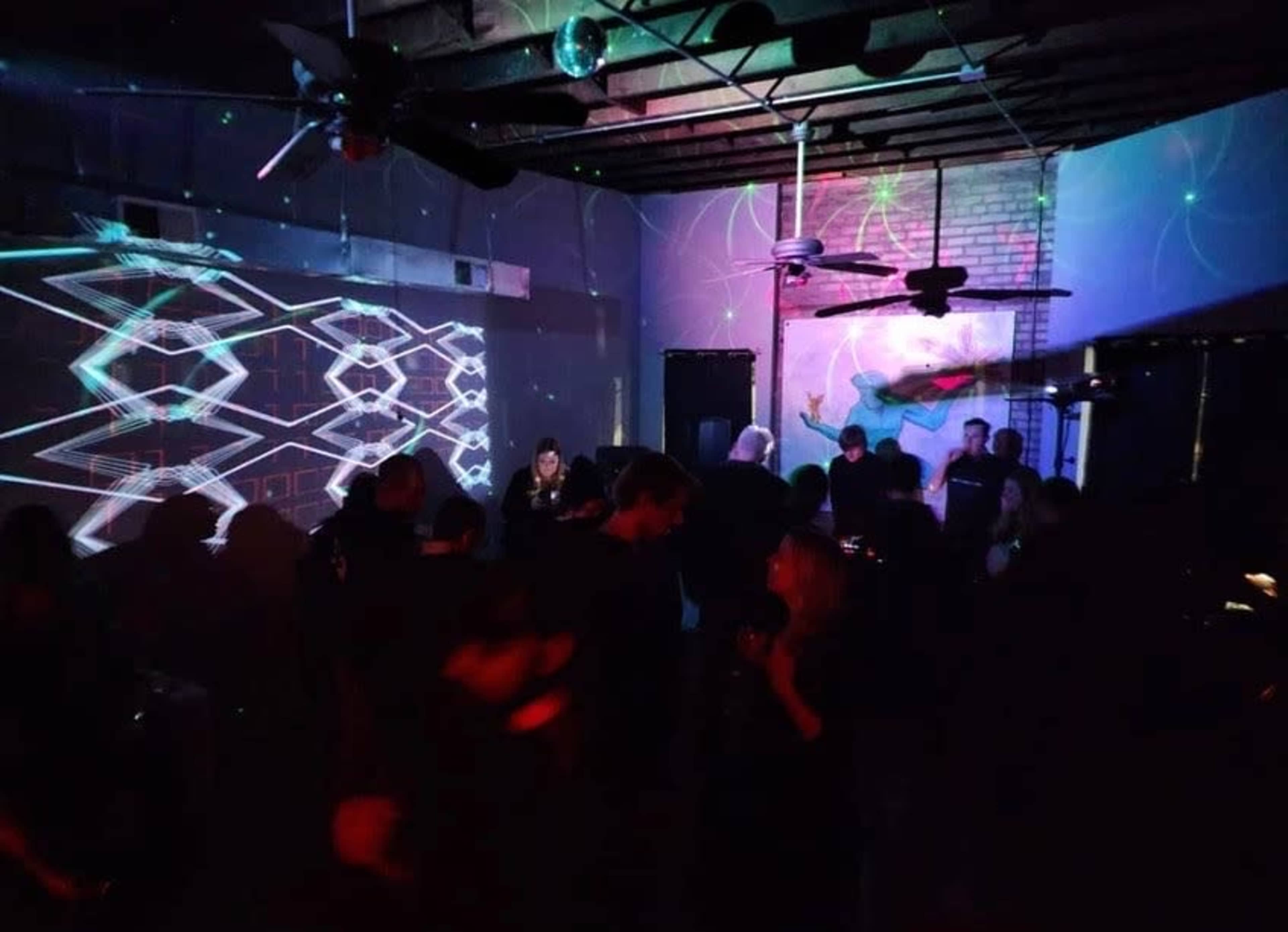 A dimly lit indoor space with people dancing and colorful light projections on the walls.