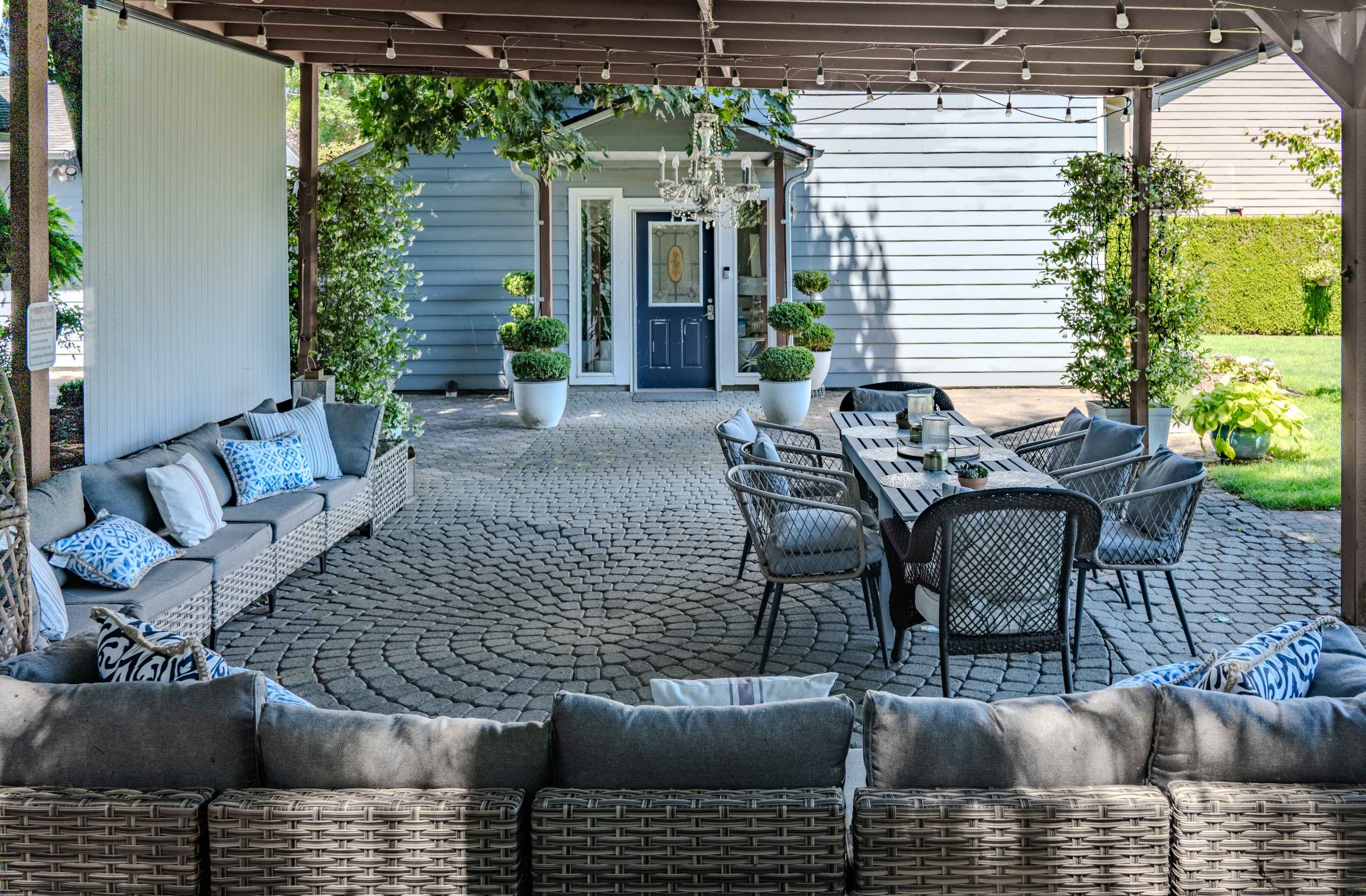 A patio area features a large sectional sofa, a dining table with chairs, and decorative potted plants under a pergola.
