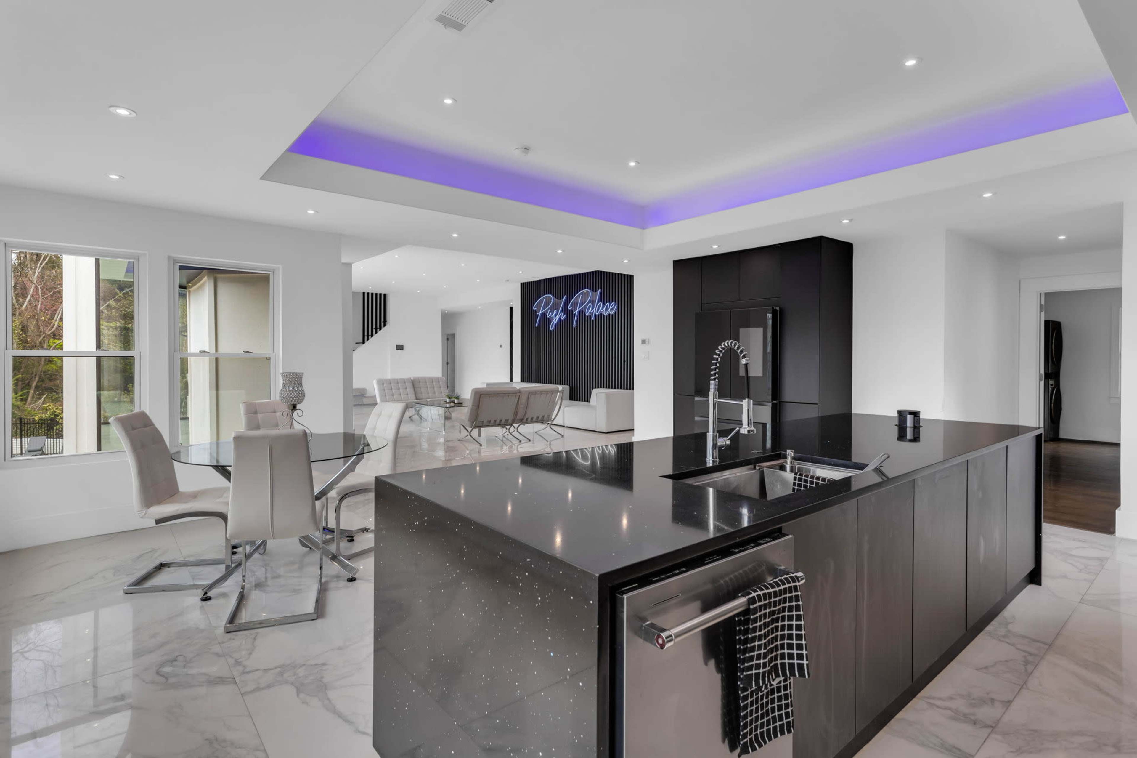 A modern kitchen and dining area featuring a large island with a black countertop, sleek cabinetry, and glass dining chairs.