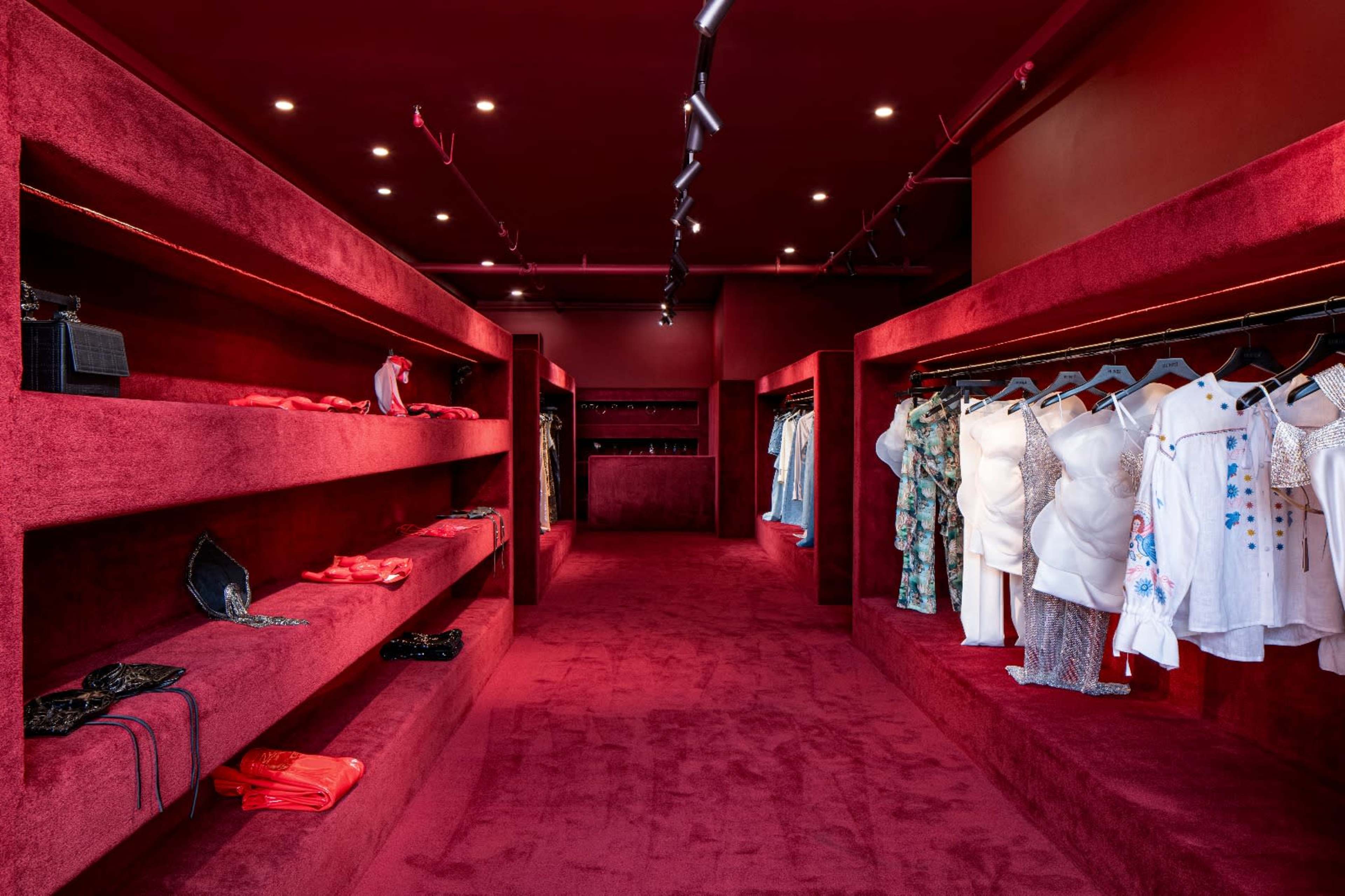 A clothing boutique features shelves lined with apparel and accessories, all set against deep red walls and carpet.