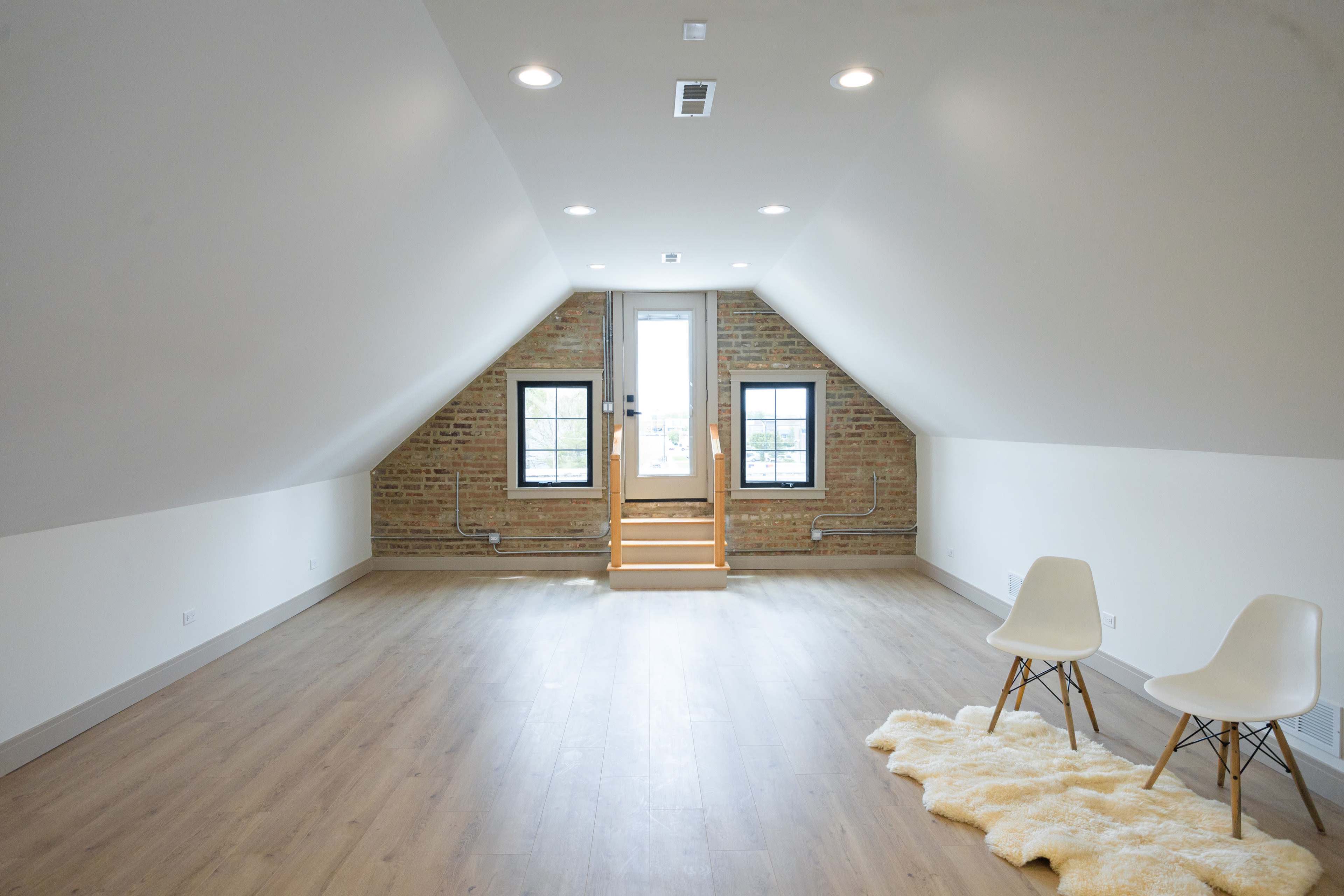 The image shows a spacious, airy attic with sloped ceilings, a wooden floor, and a doorway leading to an outdoor area.