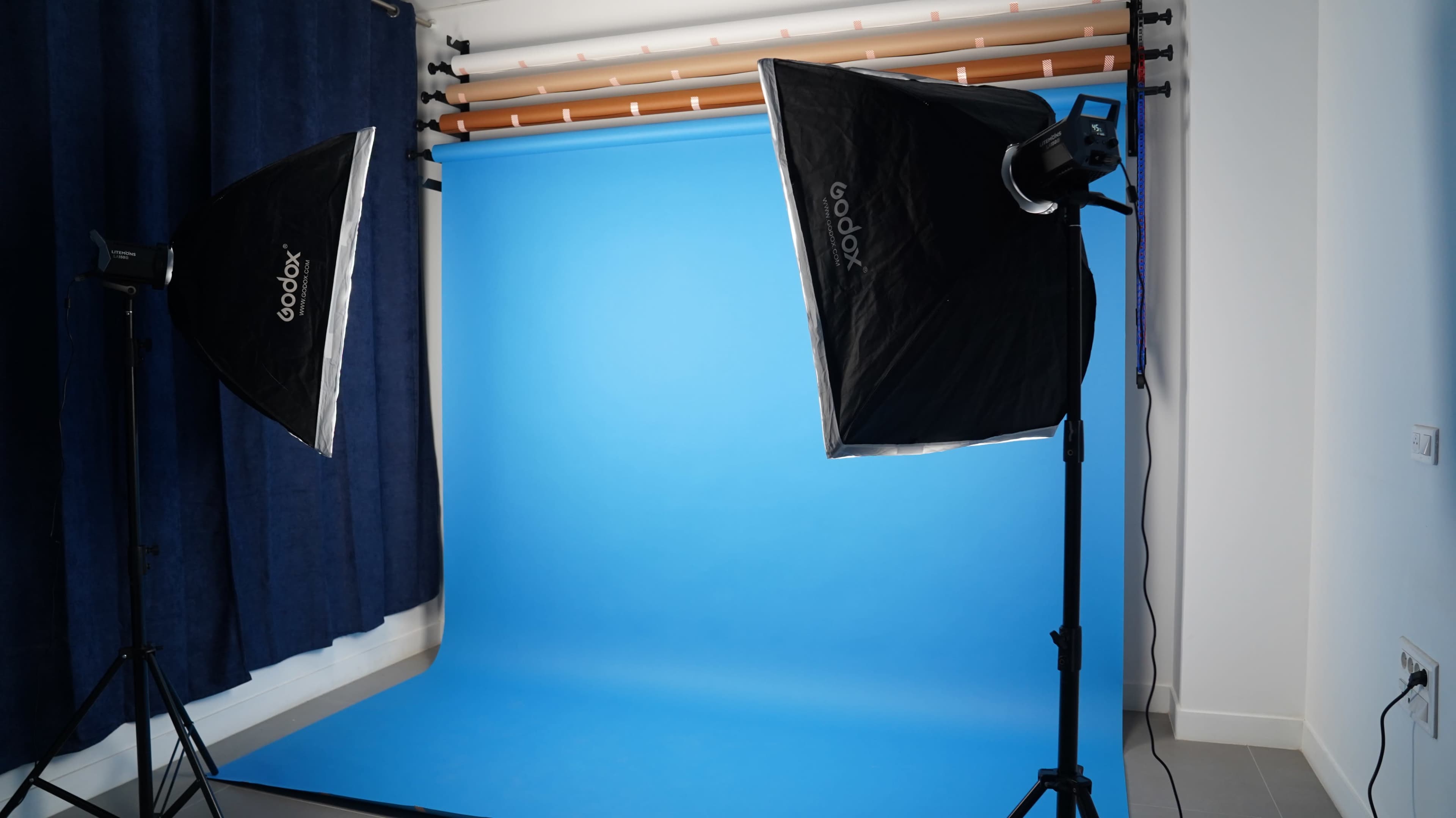 The image shows a photography studio setup with two softbox lights positioned on either side of a vibrant blue backdrop.