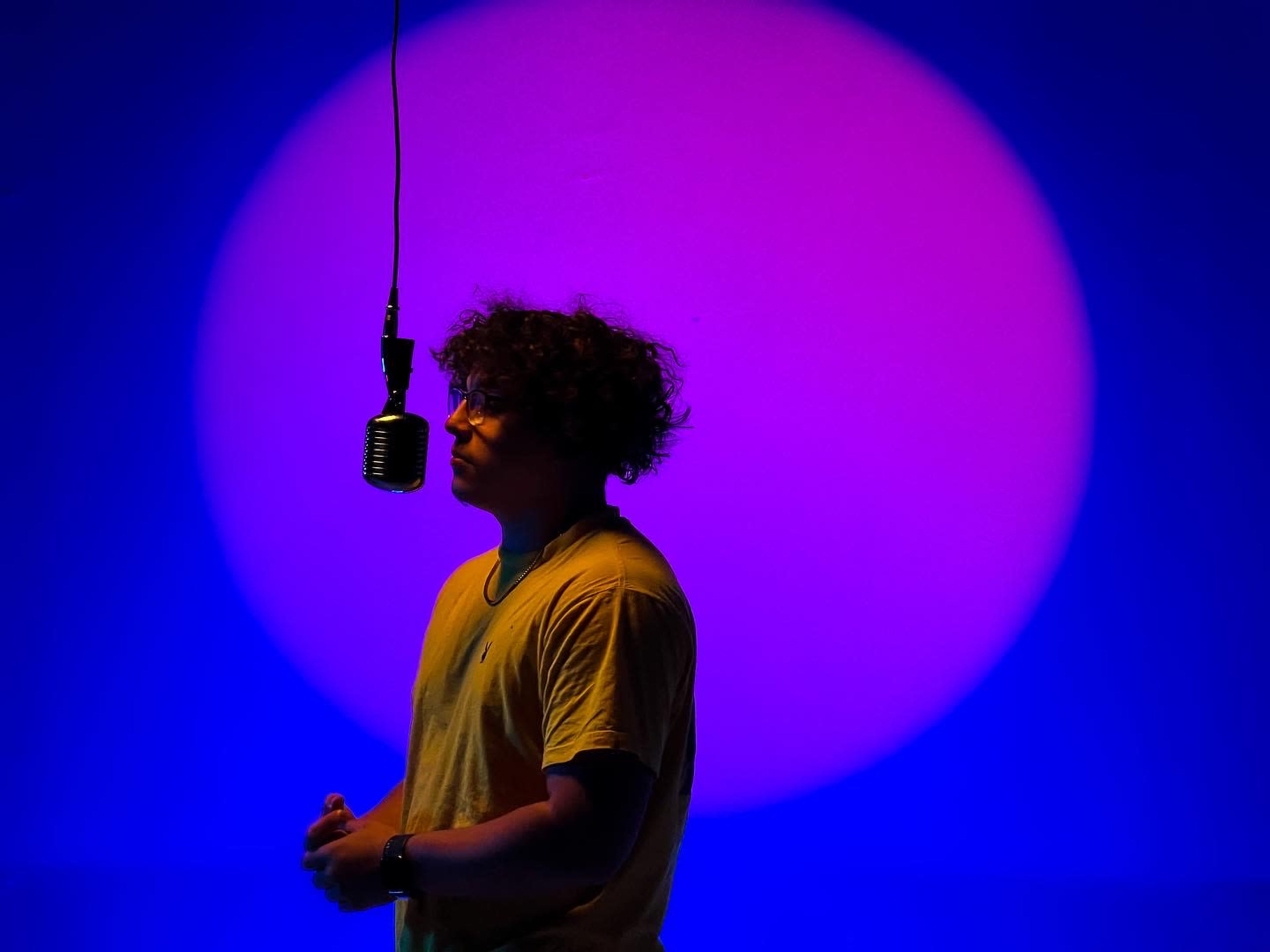 A silhouetted figure stands in front of a microphone against a colorful, gradient background.