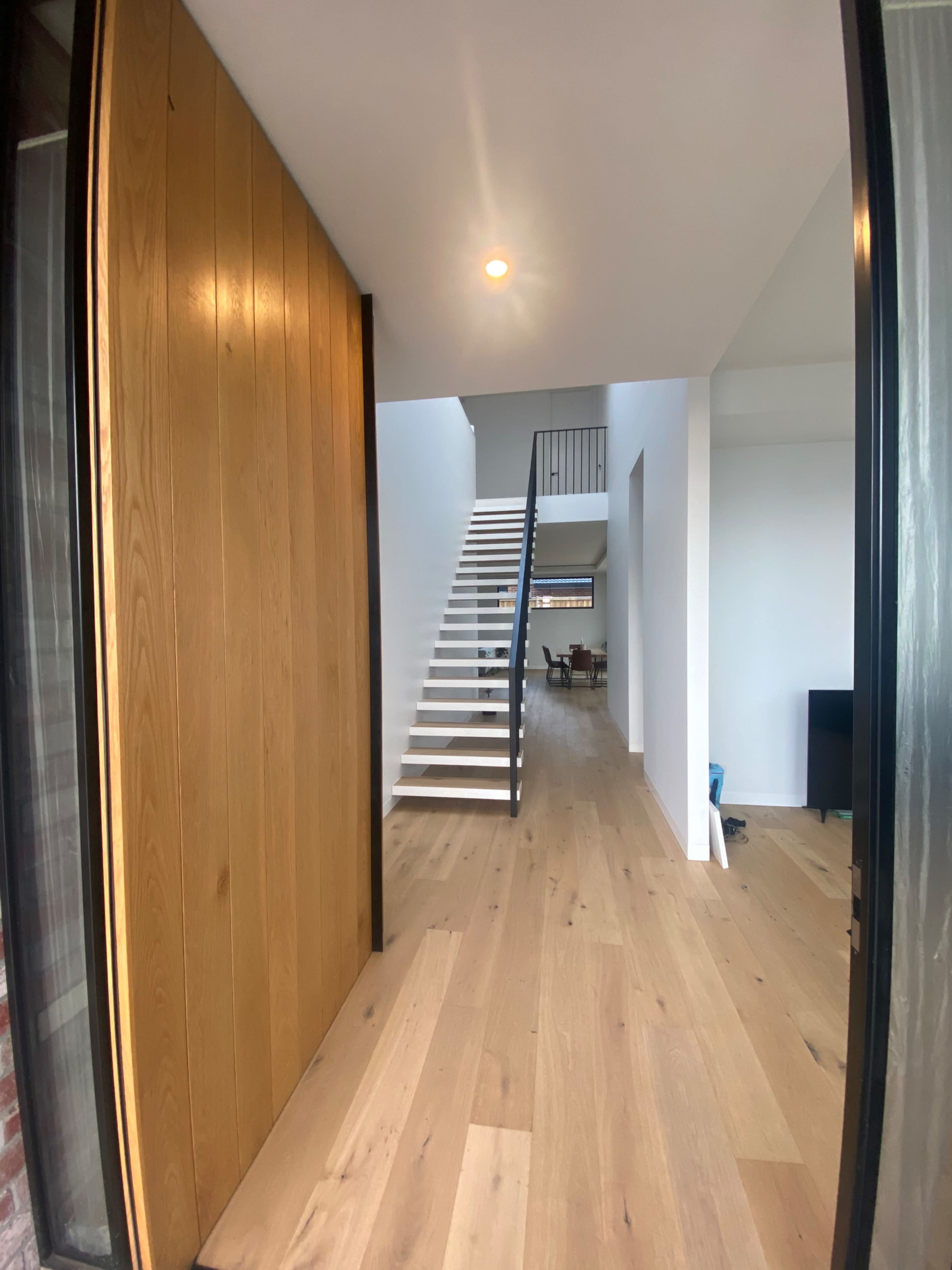 A wooden front door opens to a modern interior with a staircase and an unobstructed view of a clean, spacious living area.