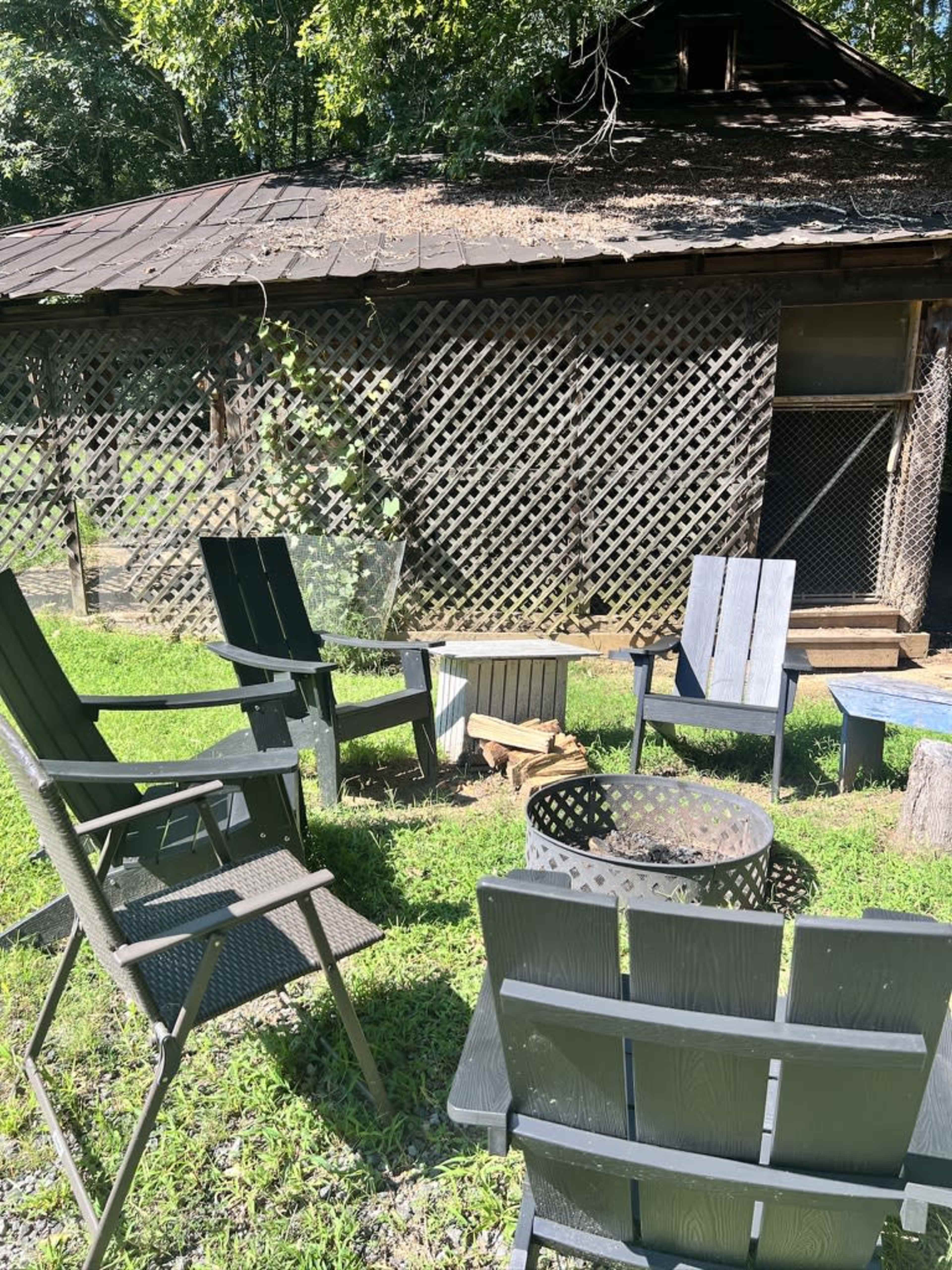 The image shows several chairs arranged around a small fire pit in a grassy area near a wooden structure with a lattice wall.