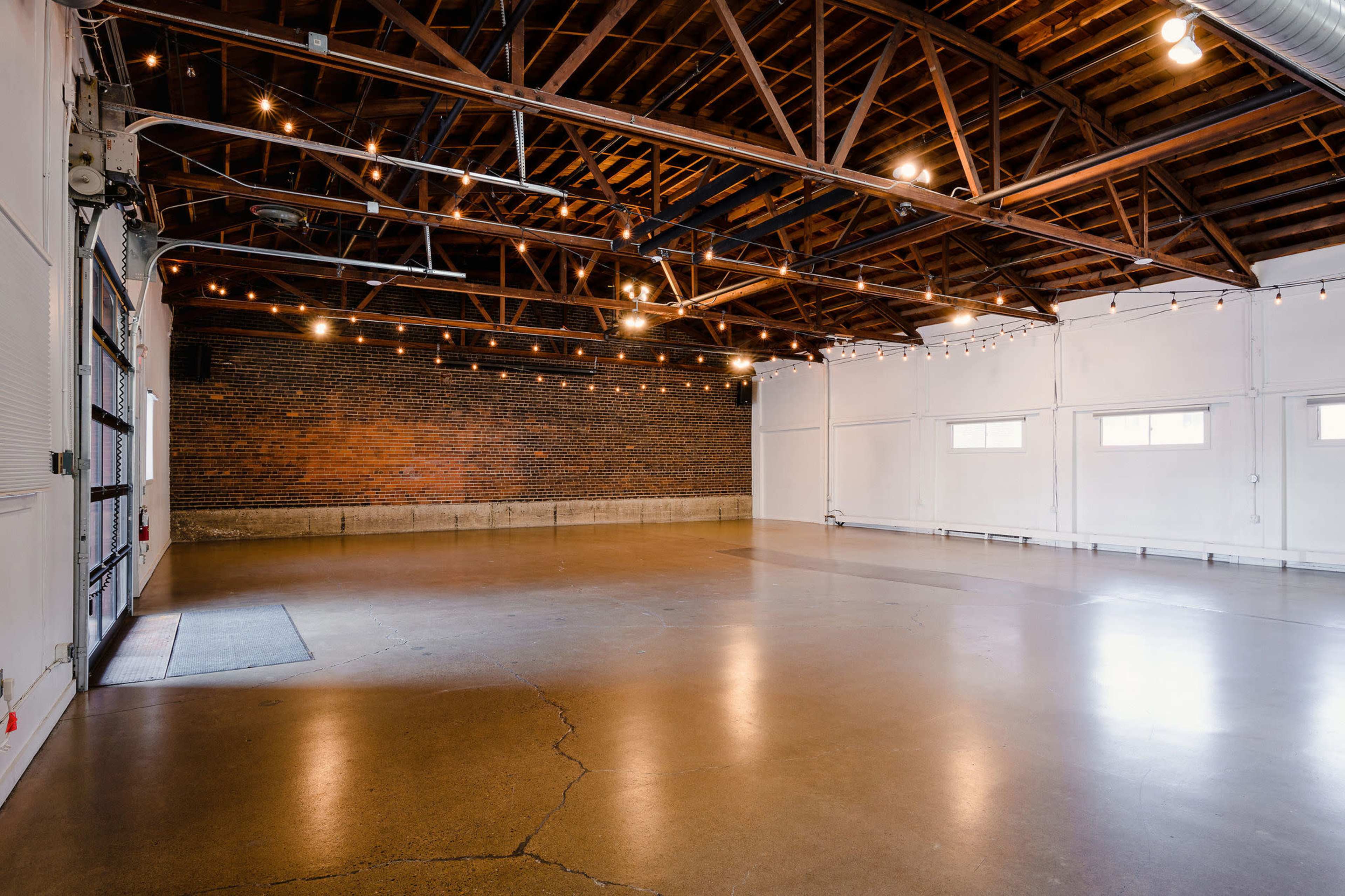 An empty event space with exposed brick walls, high wooden ceilings, and industrial-style lighting.