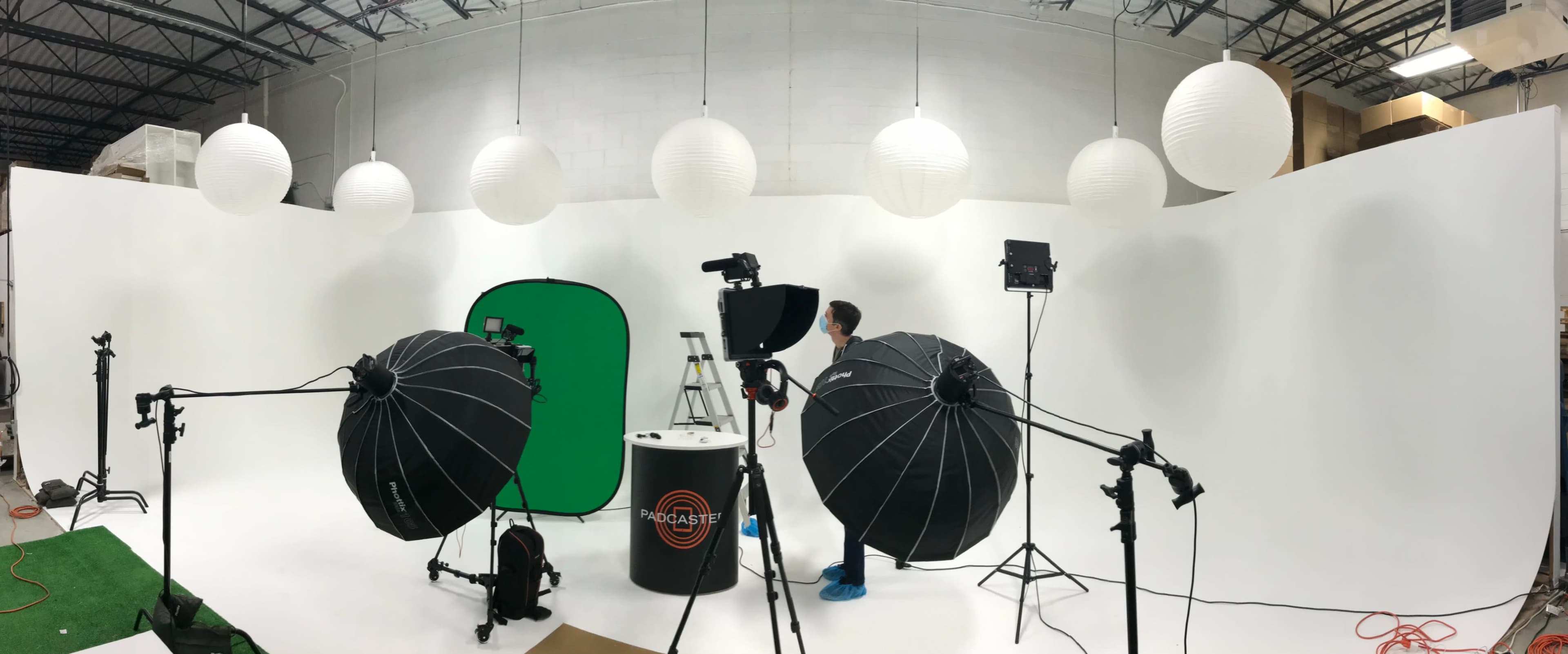 A photography studio features a green screen setup, softbox lighting, and paper lanterns hanging from the ceiling.