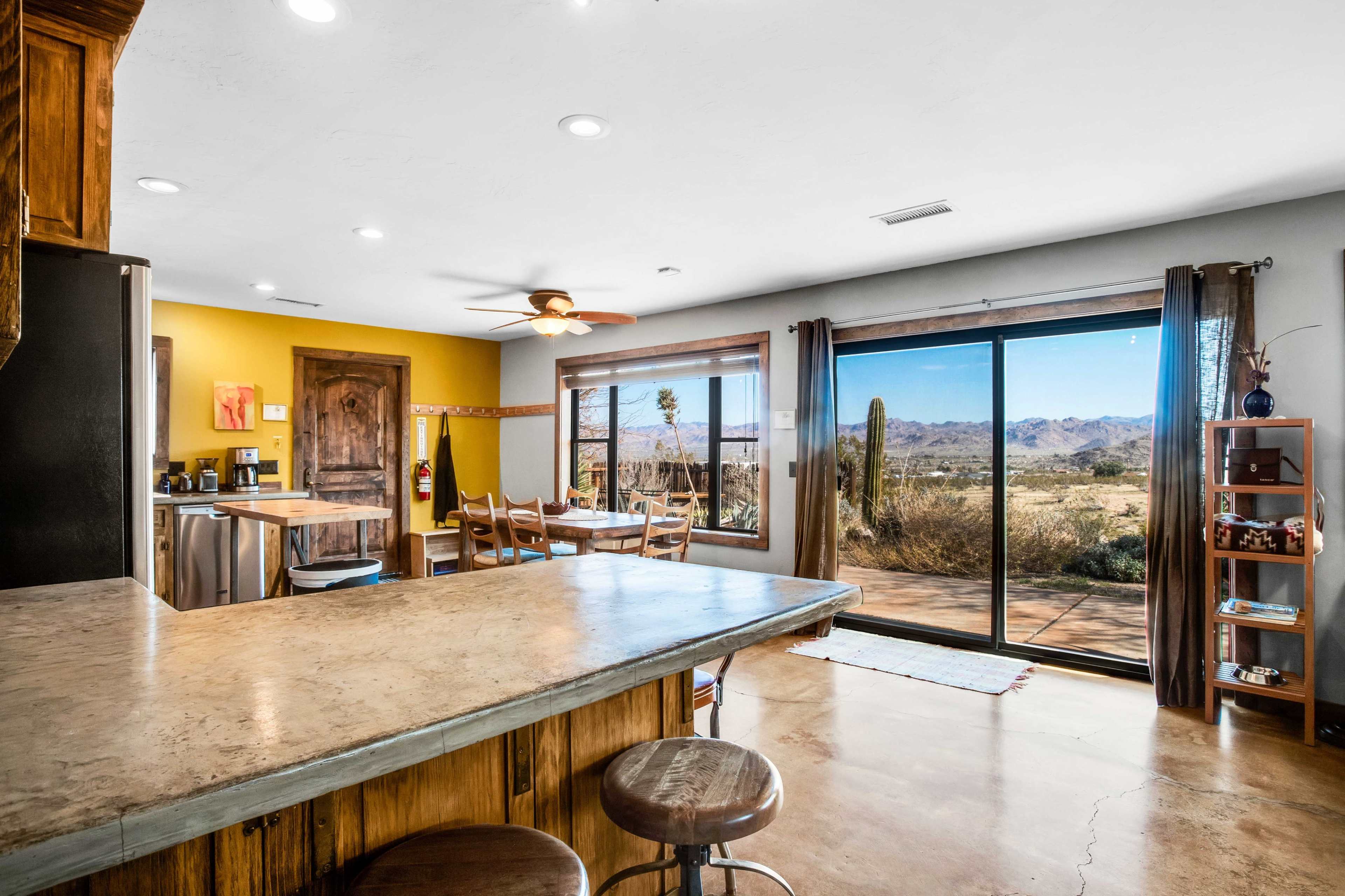 The image shows a kitchen and dining area with a sliding glass door that opens to a desert landscape.