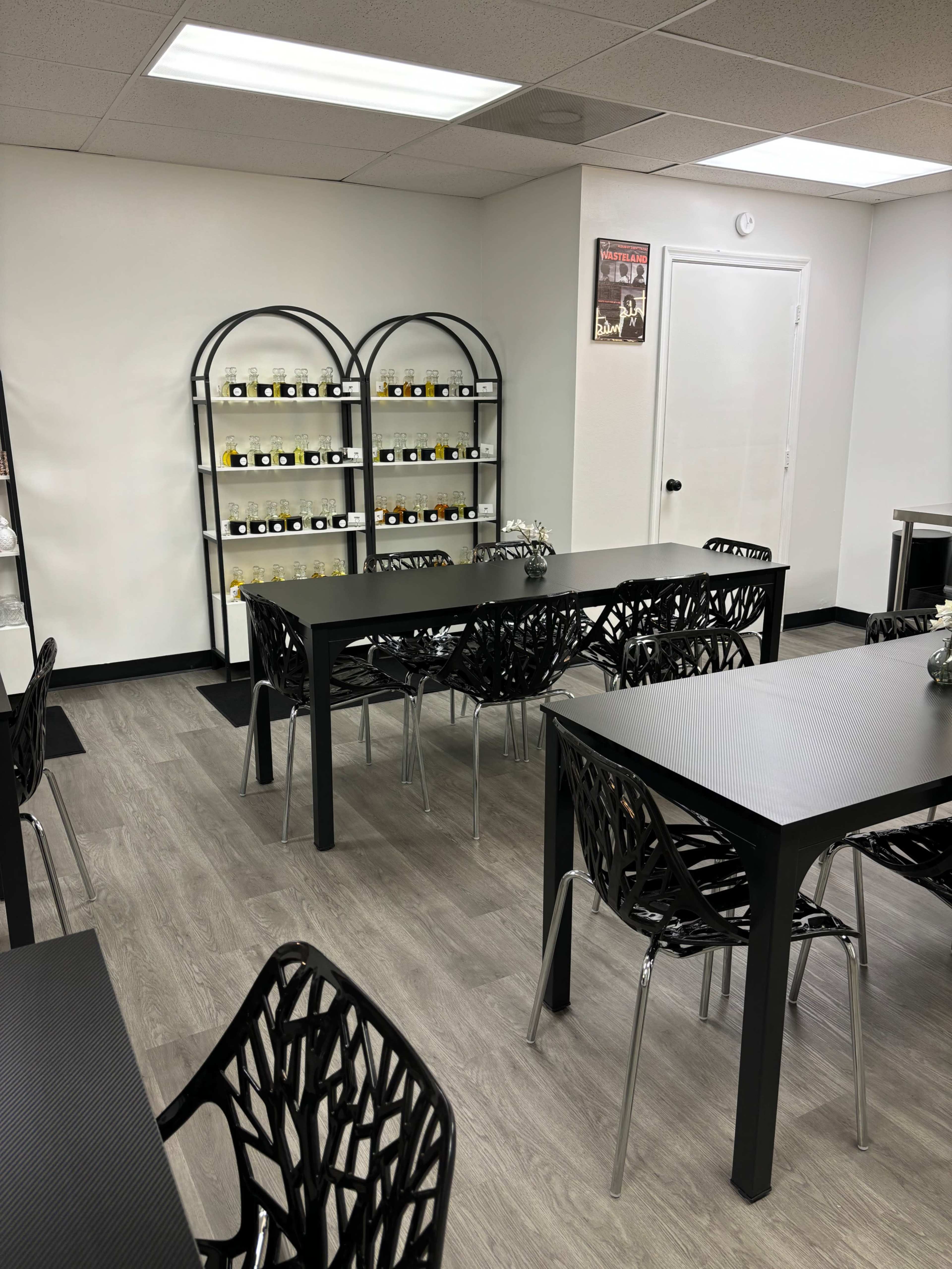 A well-lit room with black tables and chairs arranged around the space, featuring shelves filled with jars on display against a white wall.