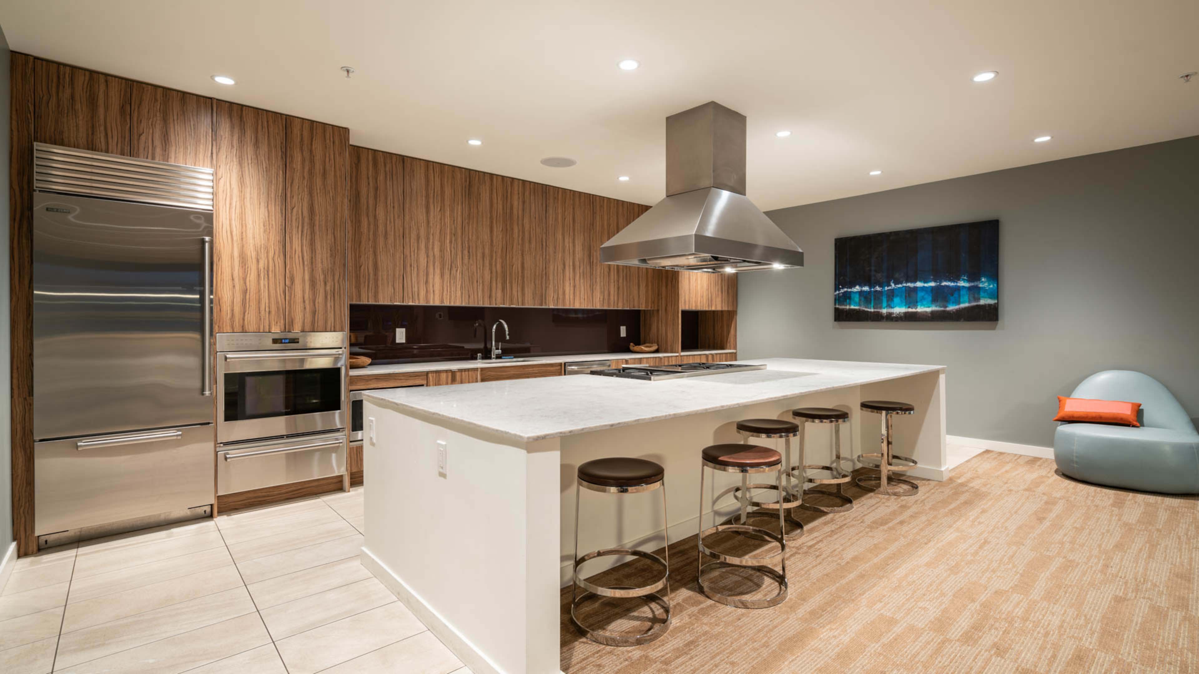 A modern kitchen featuring a large island with bar stools, stainless steel appliances, and wooden cabinetry.