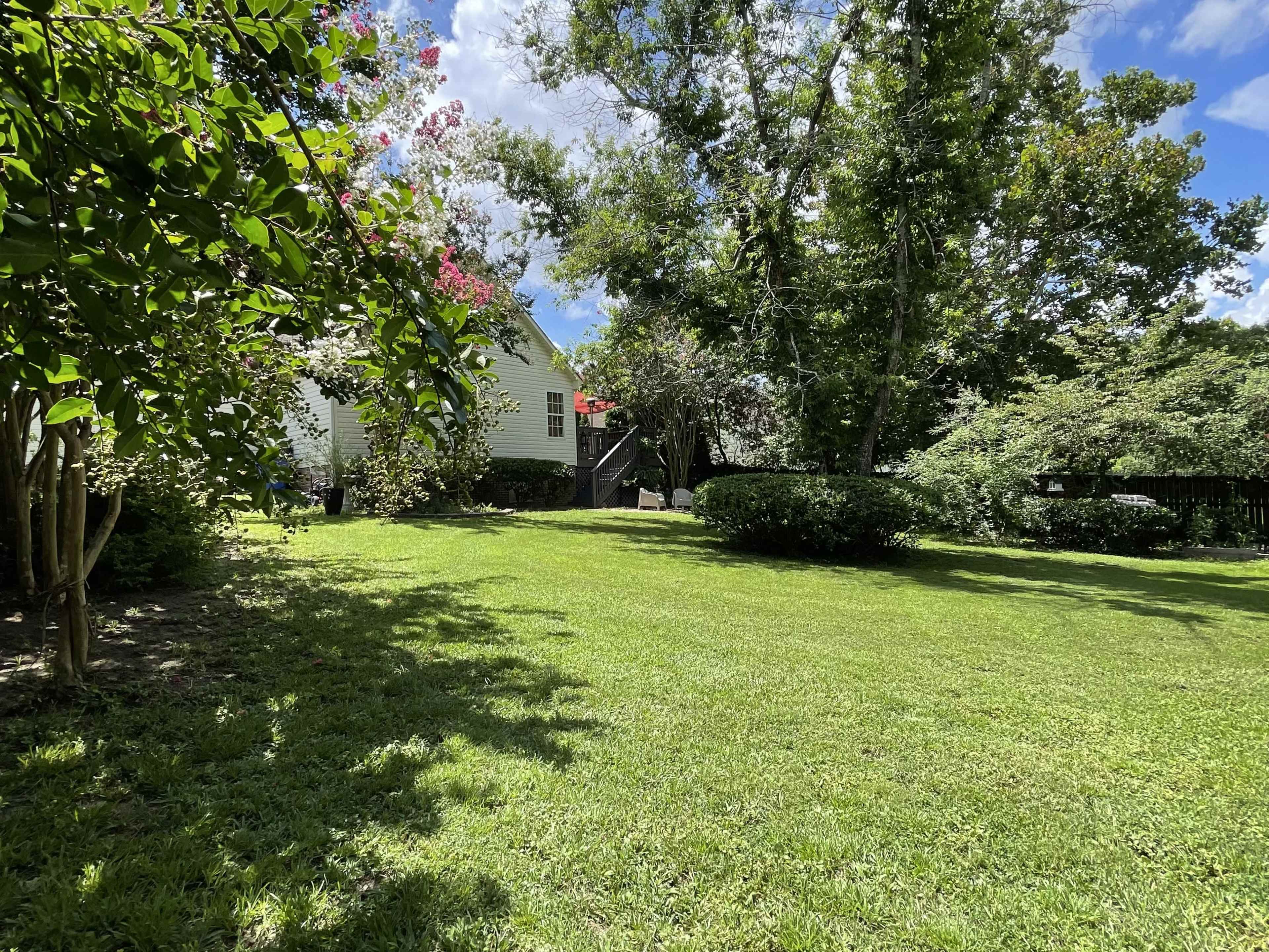 A well-maintained backyard features a lawn, leafy trees, and a white house in the background.