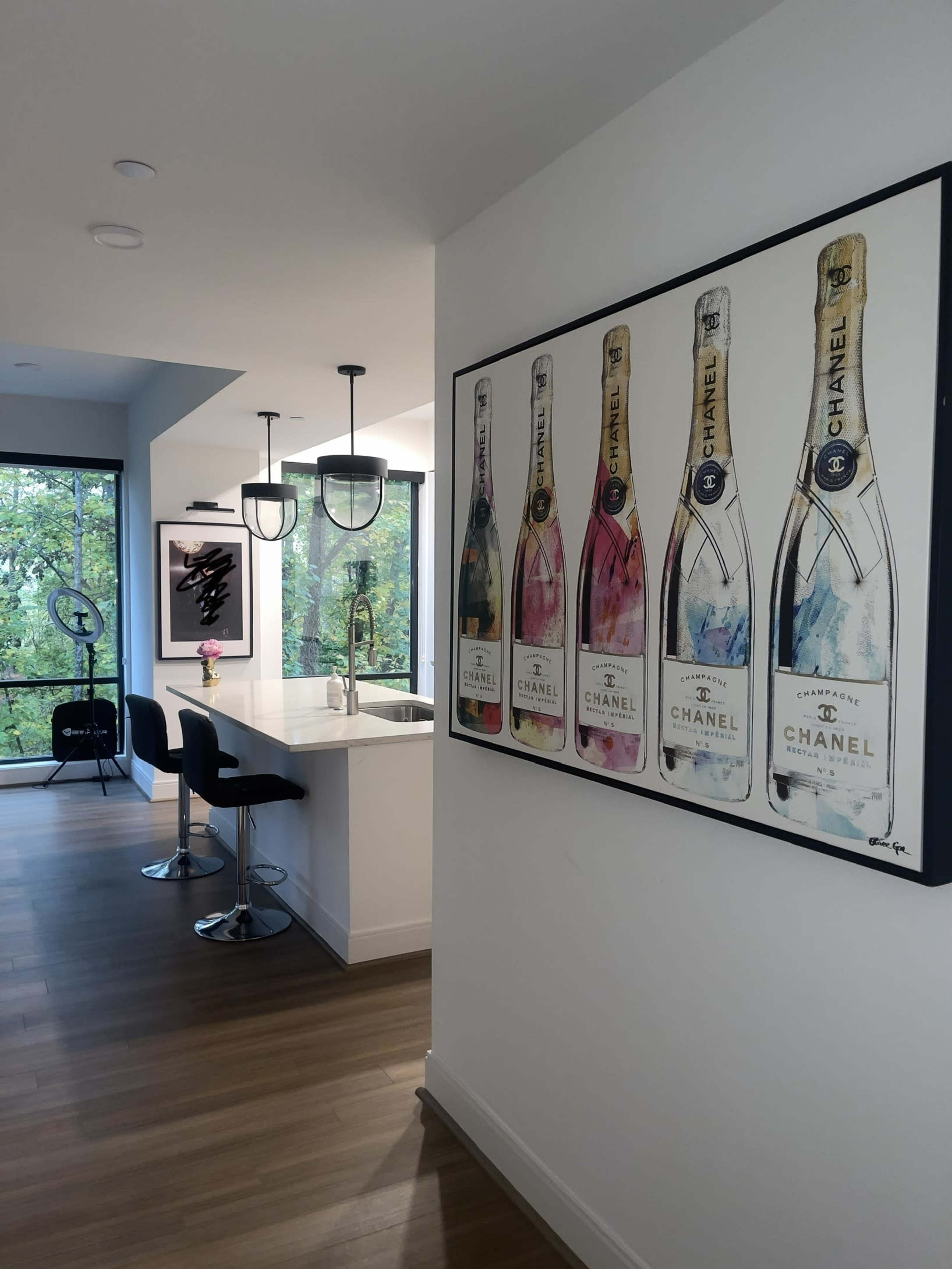 A modern kitchen with a bar area featuring black stools and a large framed artwork of champagne bottles on the wall.
