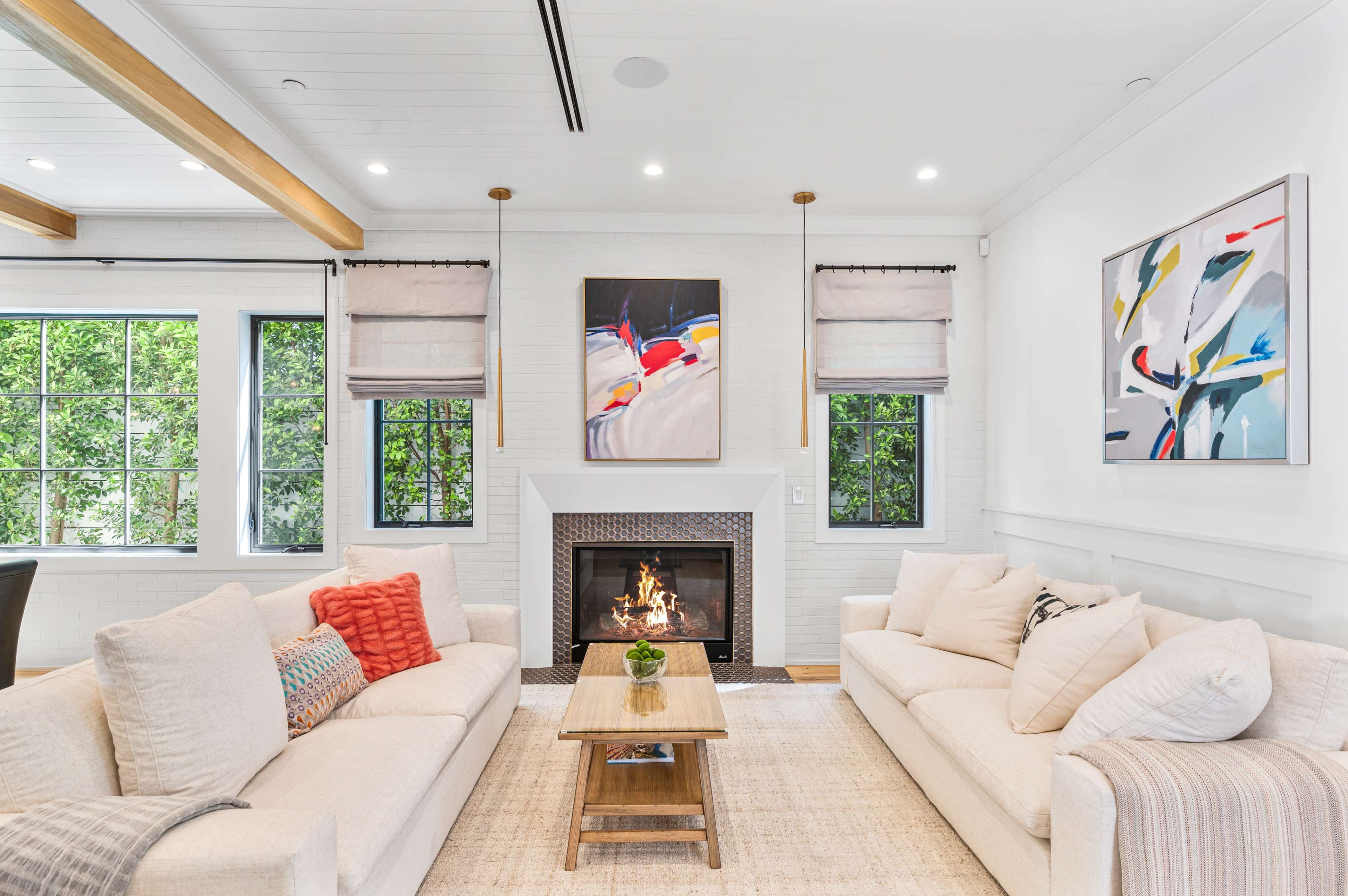 A bright living room with two sofas facing a coffee table and a fireplace flanked by large windows.