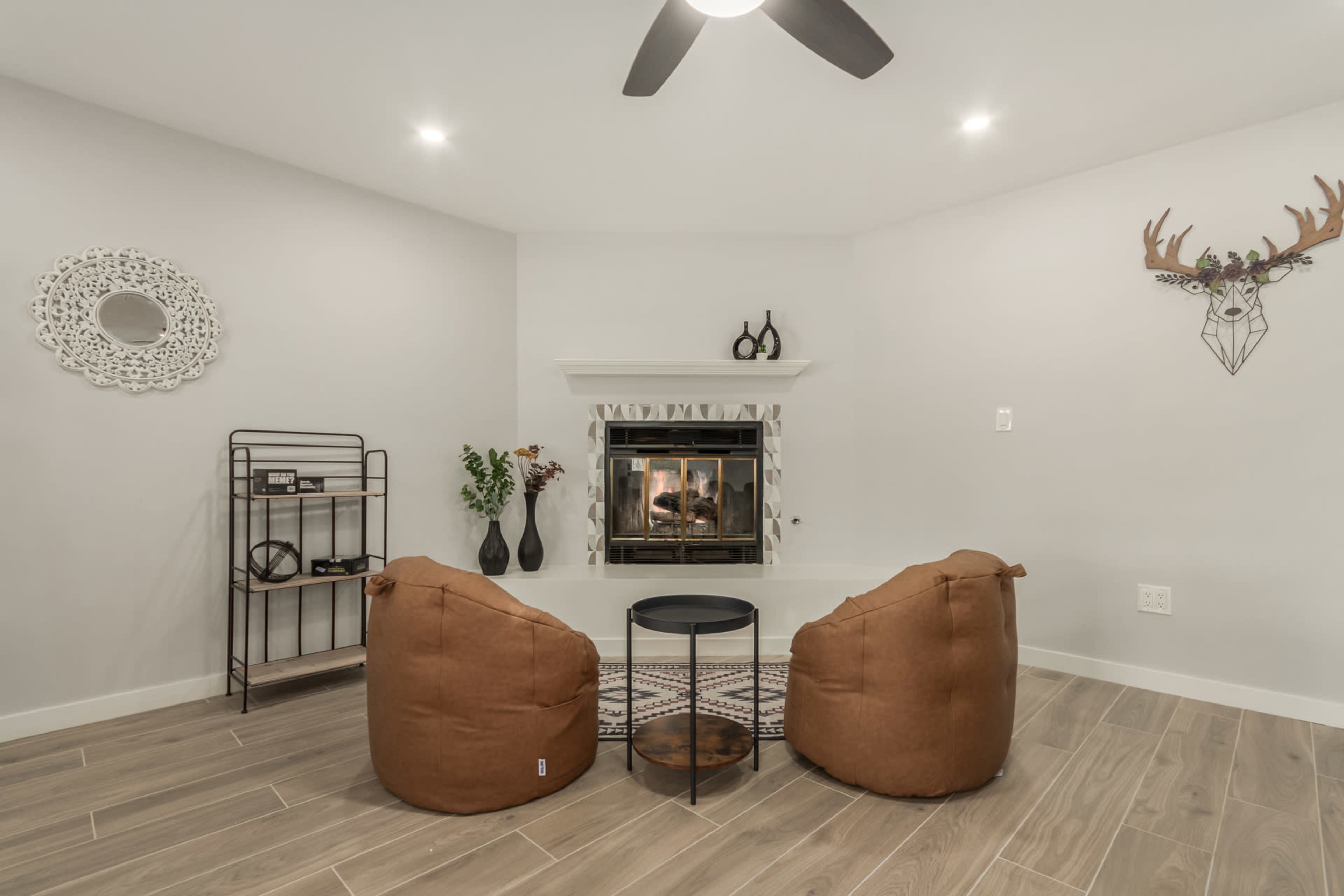 A cozy living room features two tan bean bag chairs facing a fireplace, with a small black table in between and decorative elements on the walls.