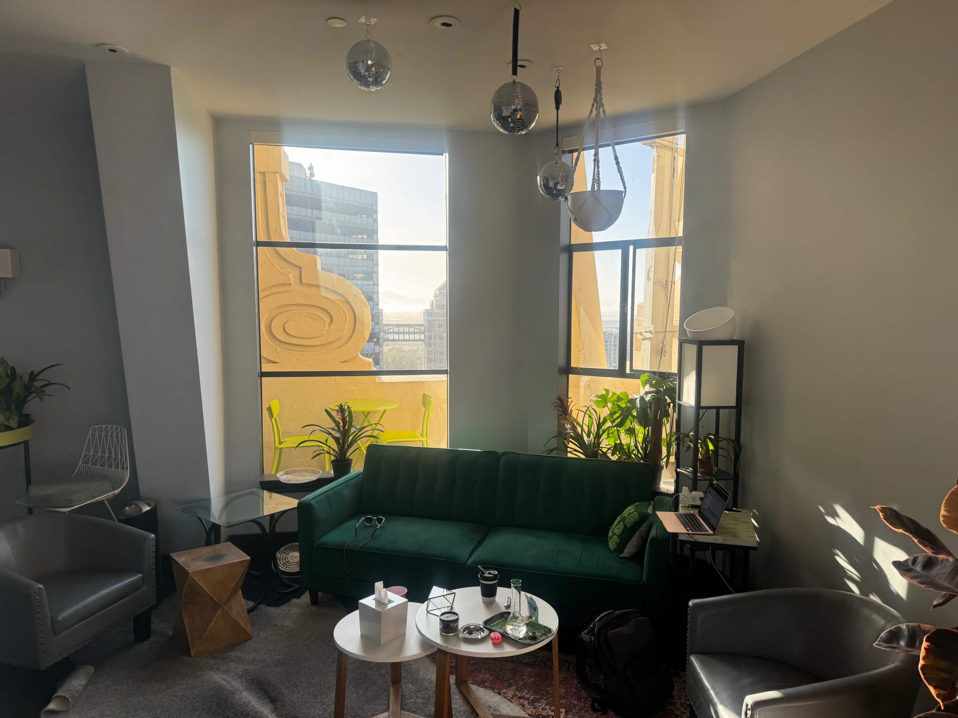 A modern living space with large windows, a green sofa, potted plants, and assorted furniture.