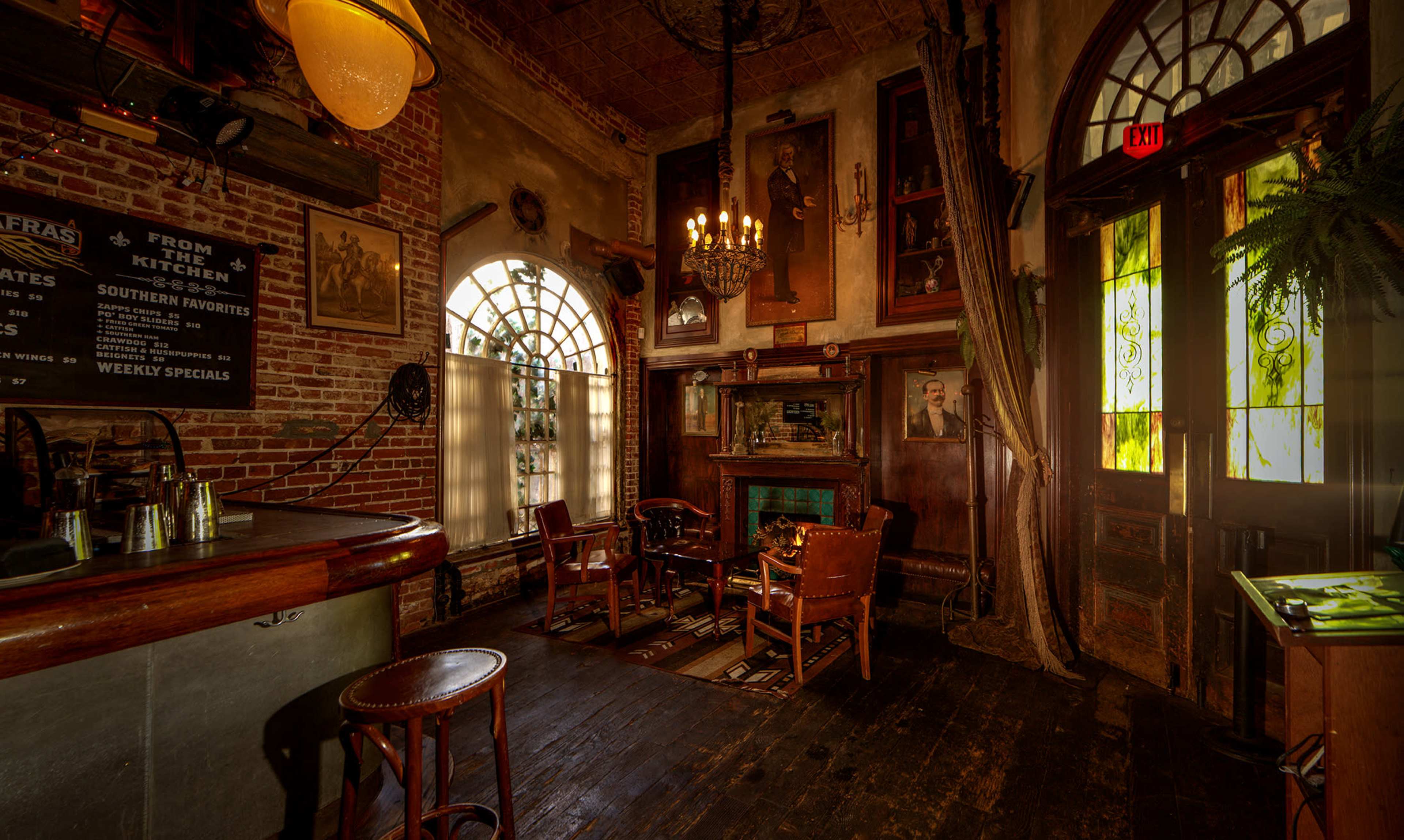 A rustic interior of a bar or restaurant featuring brick walls, wooden floors, and vintage decor, including framed portraits and a fireplace.