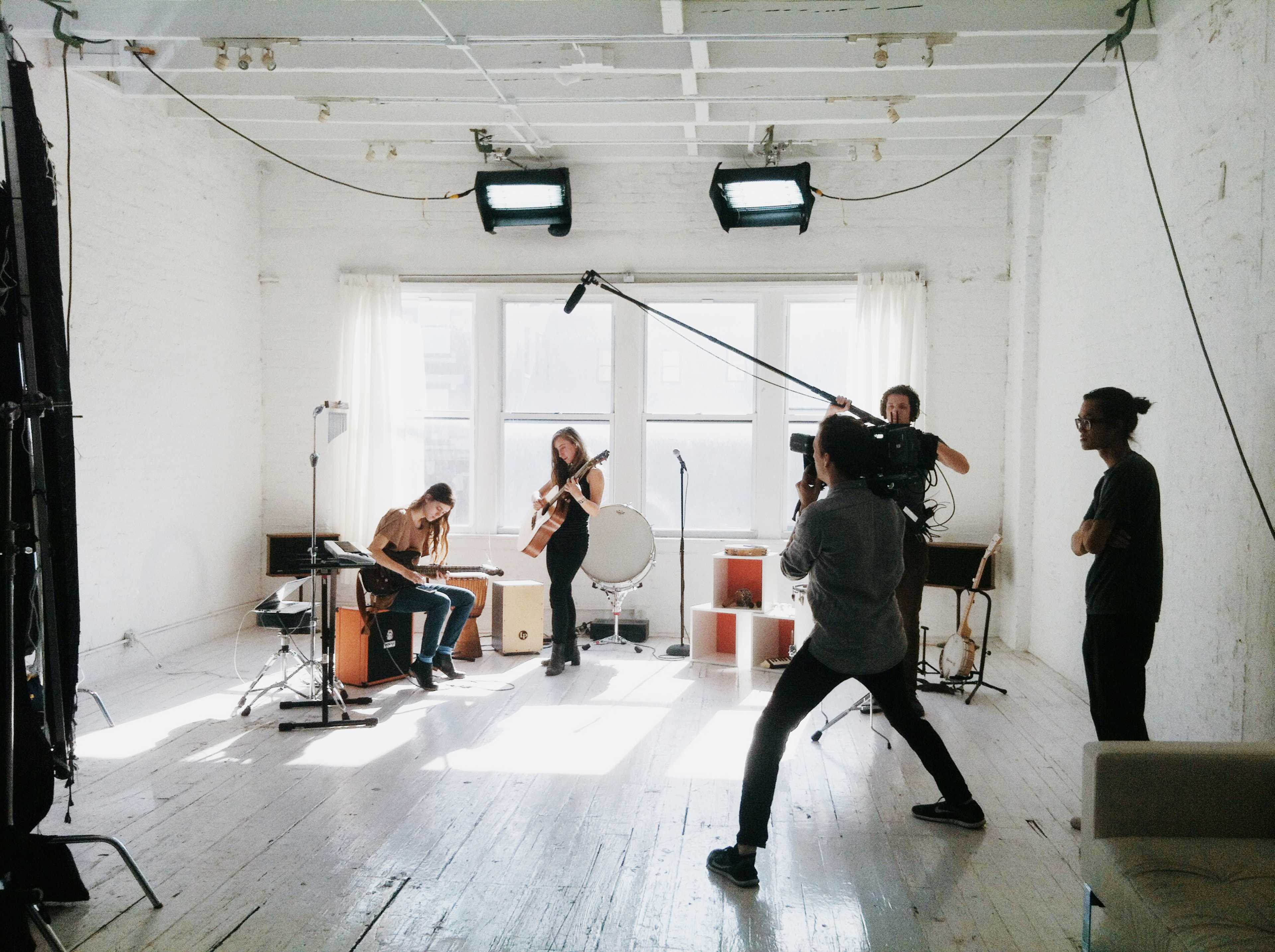 A group of musicians is performing in a well-lit studio while a videographer records the session.