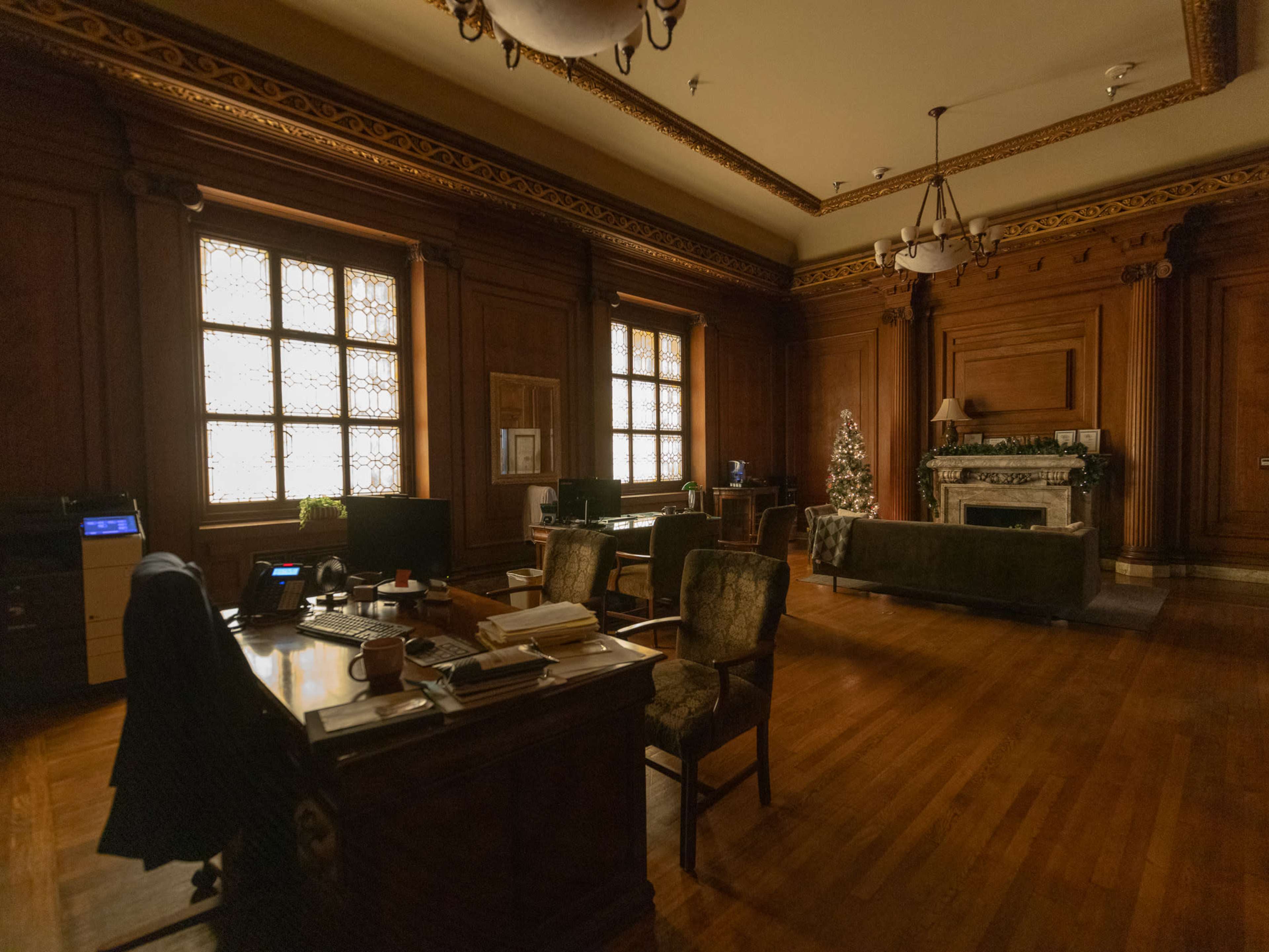 The image depicts a spacious, wooden-paneled office featuring a desk, chairs, and a decorated Christmas tree in the corner.