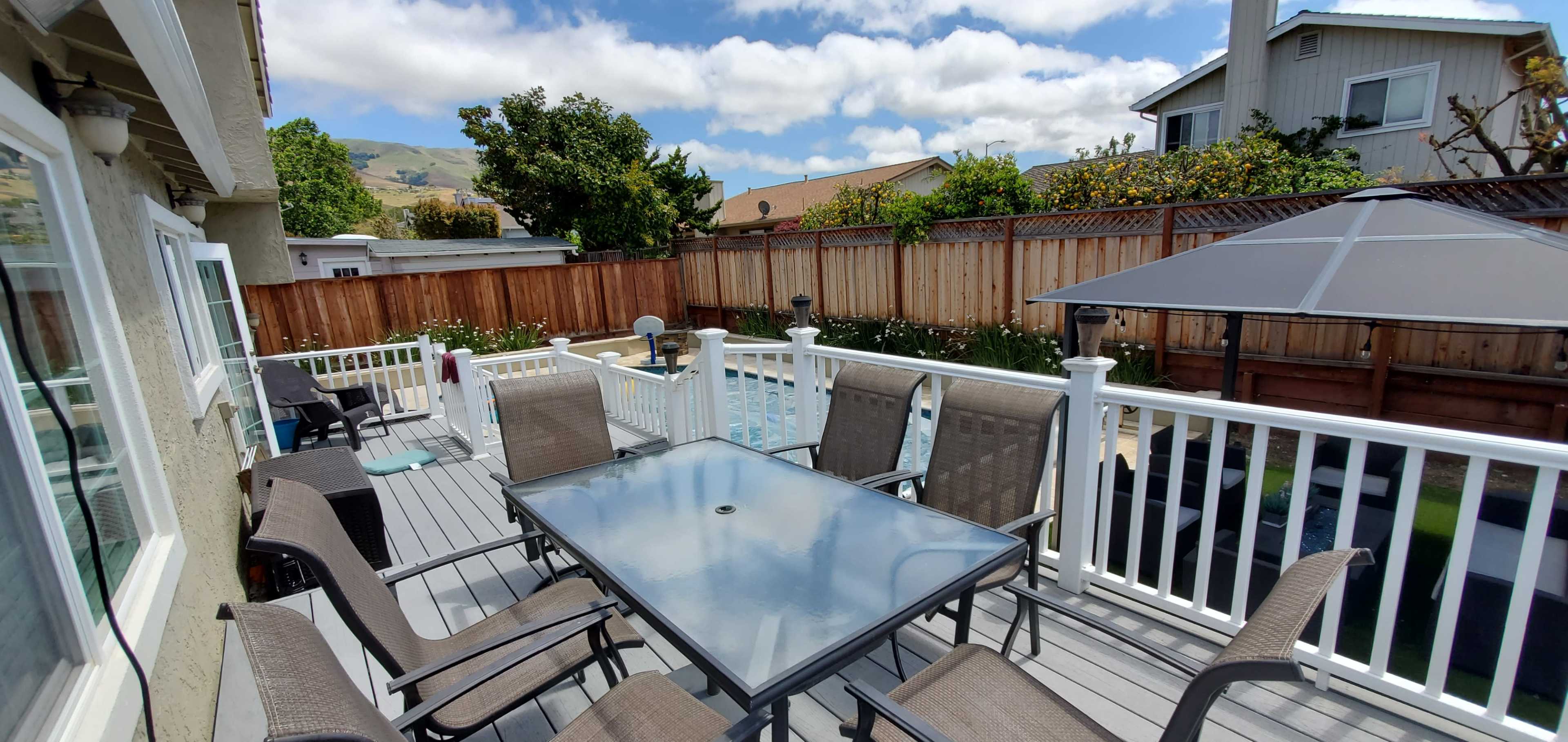 A patio area features a table surrounded by chairs, with a pool visible in the background and a patio umbrella to one side.