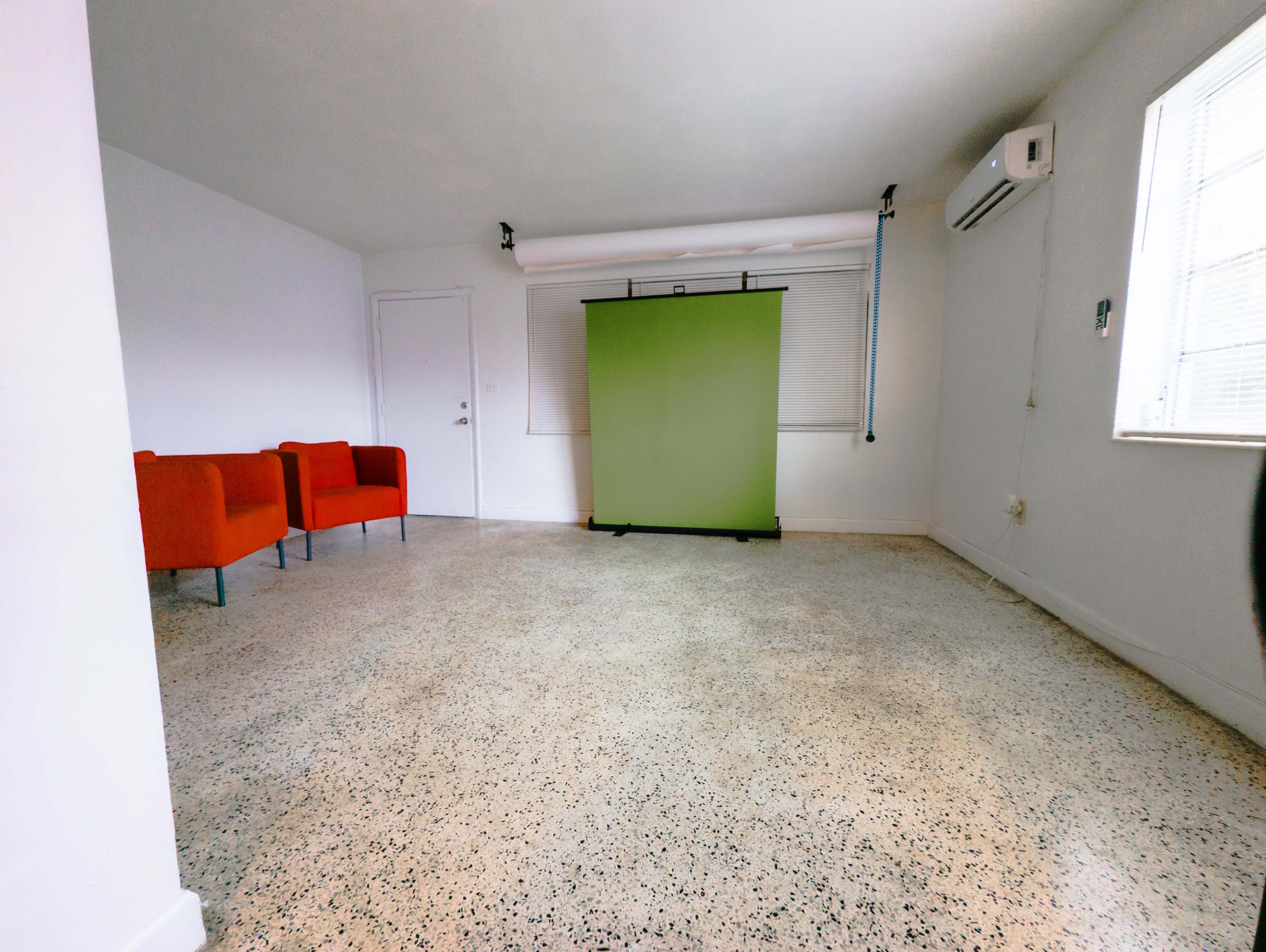 The image shows a spacious room with two red chairs, a green backdrop, and a concrete floor.