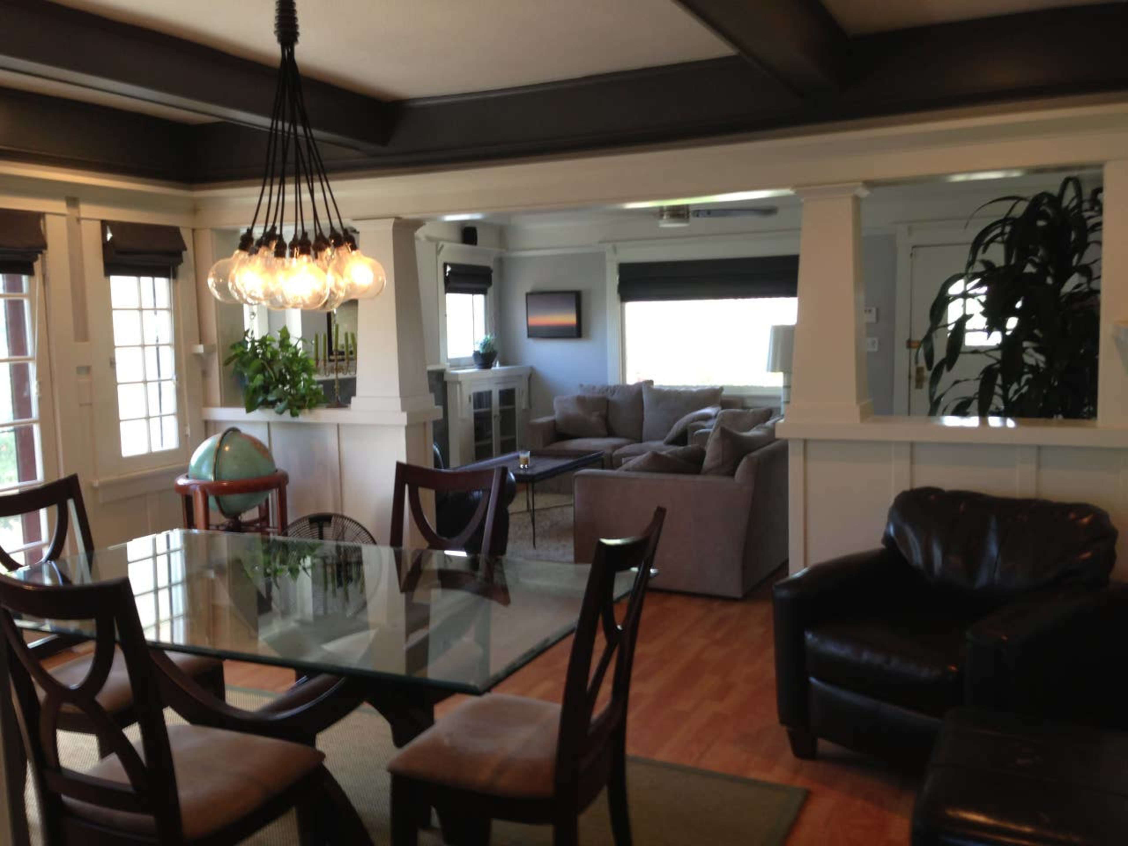 A dining area with a glass table and wooden chairs, leading into a living space with a couch and large windows.