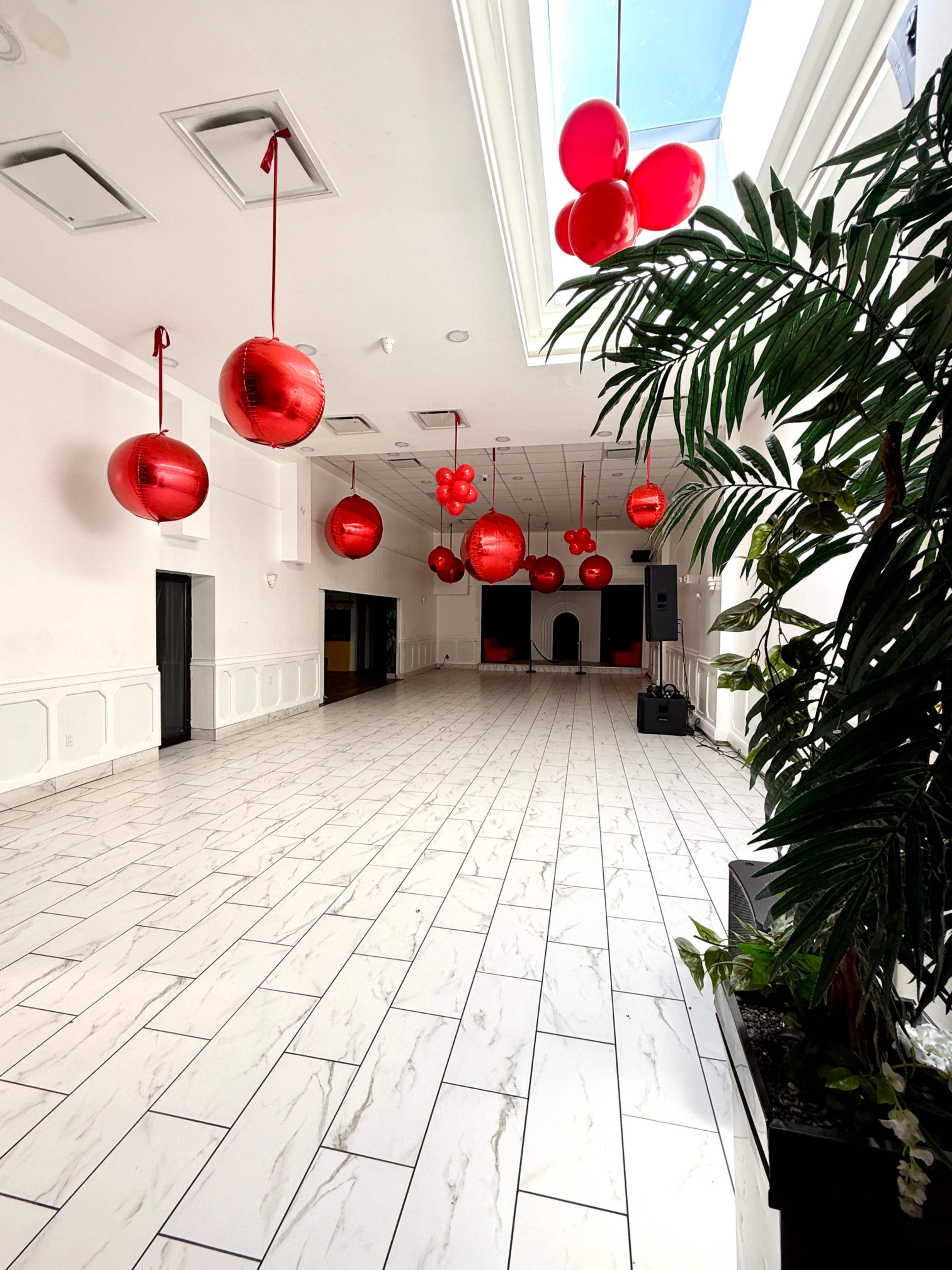 The image shows a spacious, bright room with white tiled flooring and red decorative balloons hanging from the ceiling.