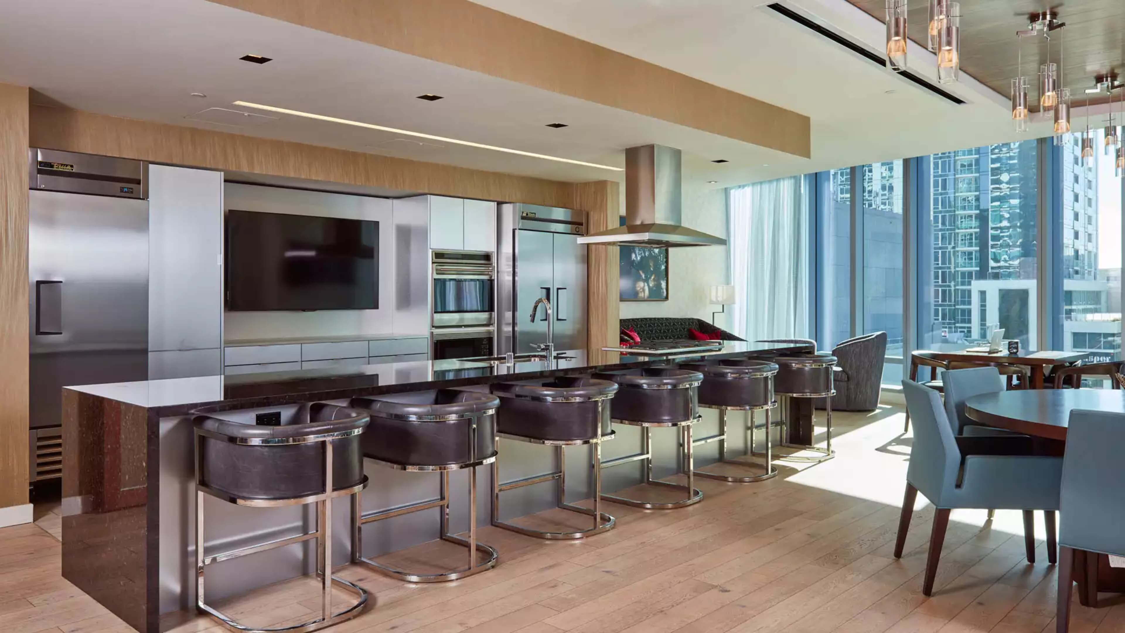 A modern kitchen with stainless steel appliances, a large island with six black bar stools, and a dining area with a round table.